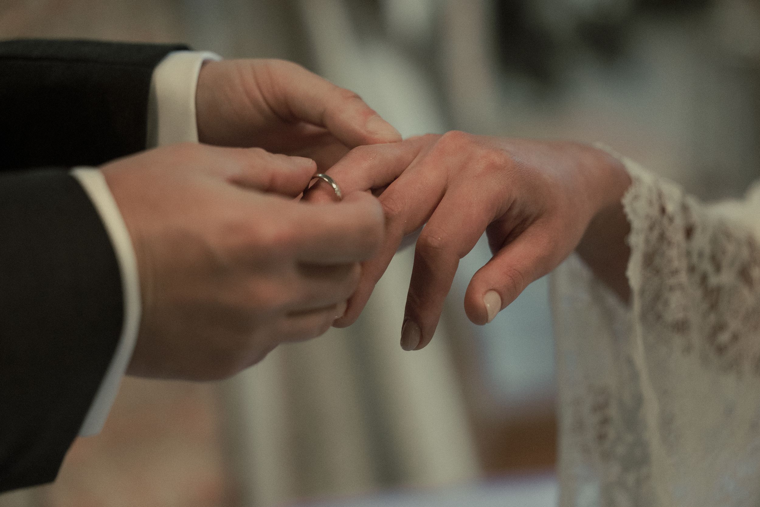 A close-up shot of hands during a wedding ceremony as a ring is being placed on a finger with lace detail visible.