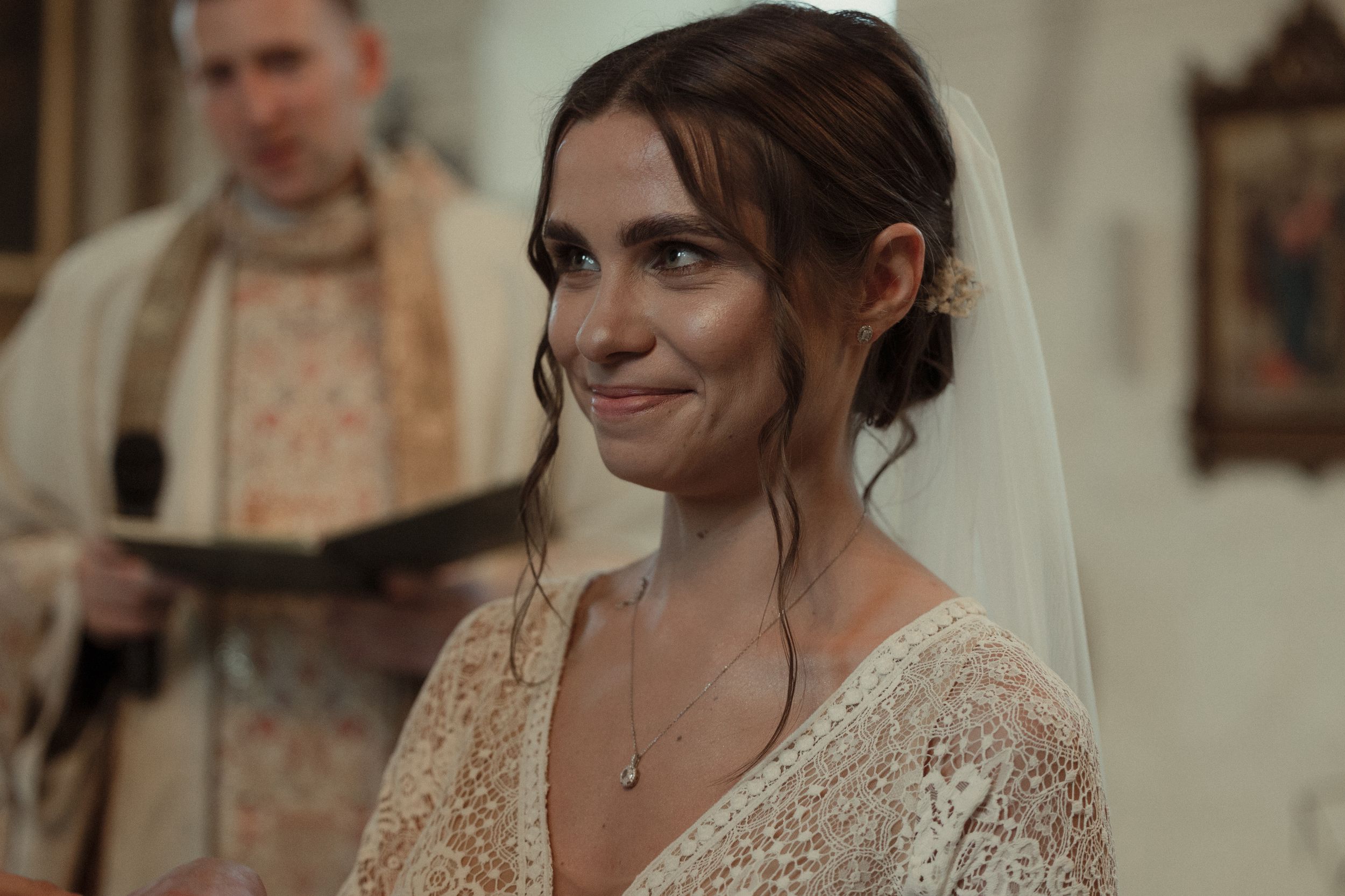 Bride wearing a loose updo hairstyle with tendrils and veil during a wedding ceremony.