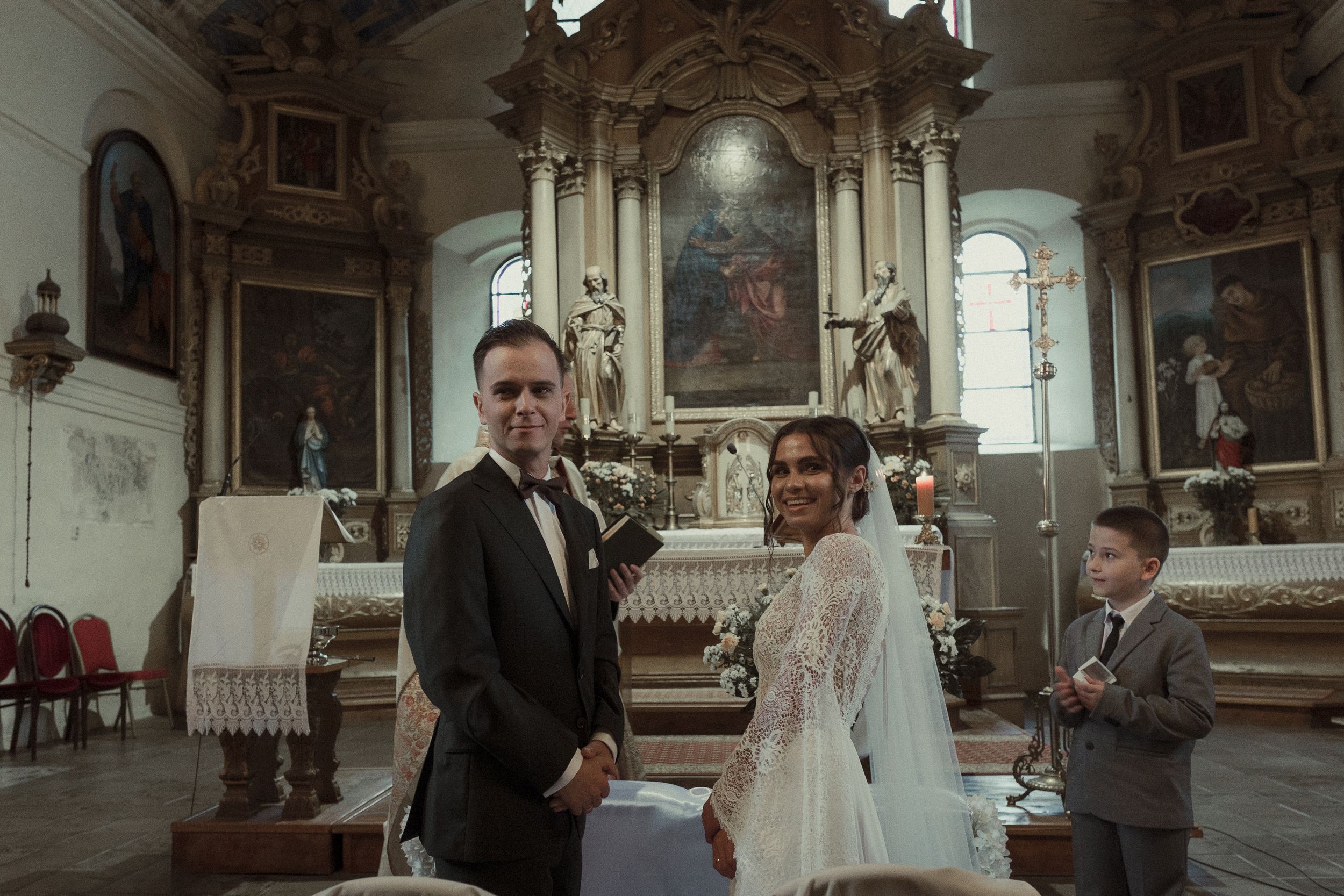 Elegant wedding ceremony takes place in an ornate historic church with high ceilings and religious artwork.