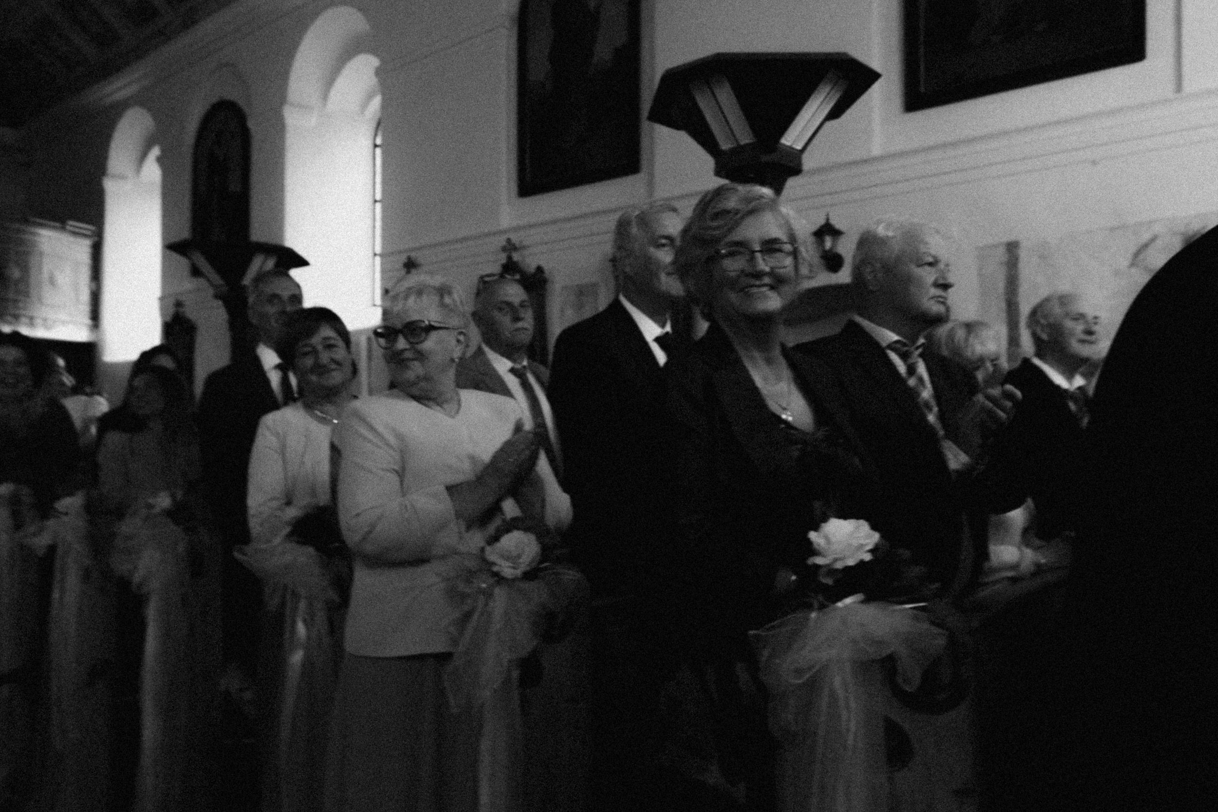 Black and white historical photograph showing a line of people in formal attire walking down an aisle during a ceremony.