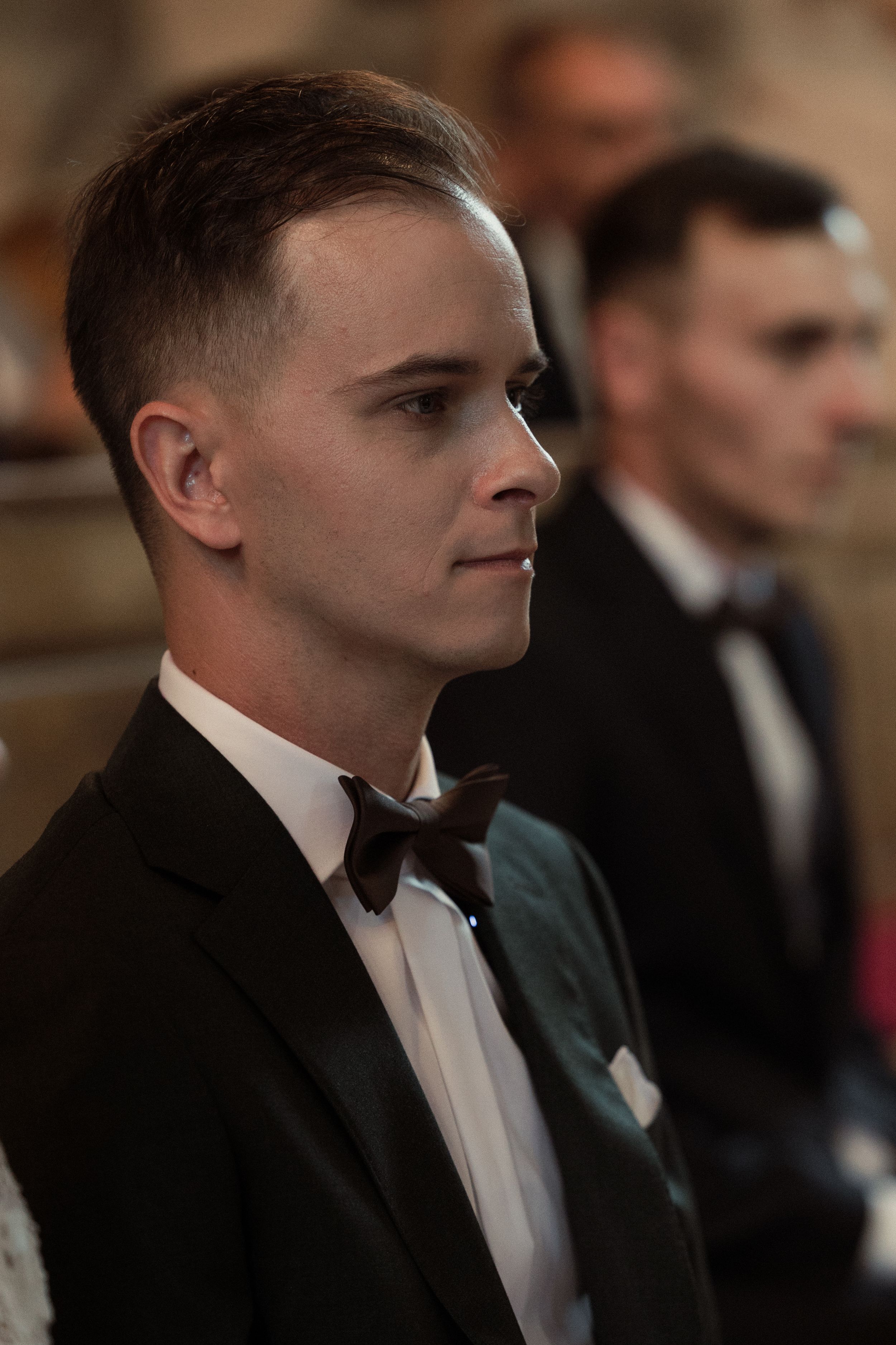 A profile view shows a person in a black bow tie and white dress shirt looking to the side during a formal event.