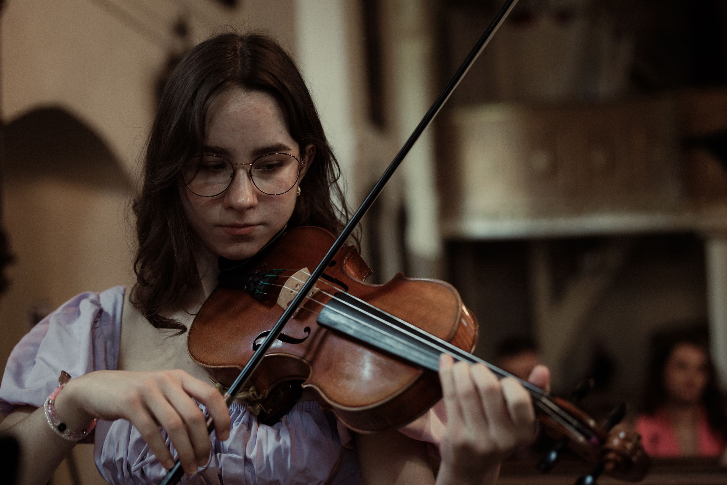 A series of photographs shows hands playing violins with bows while wearing formal attire in a concert setting.