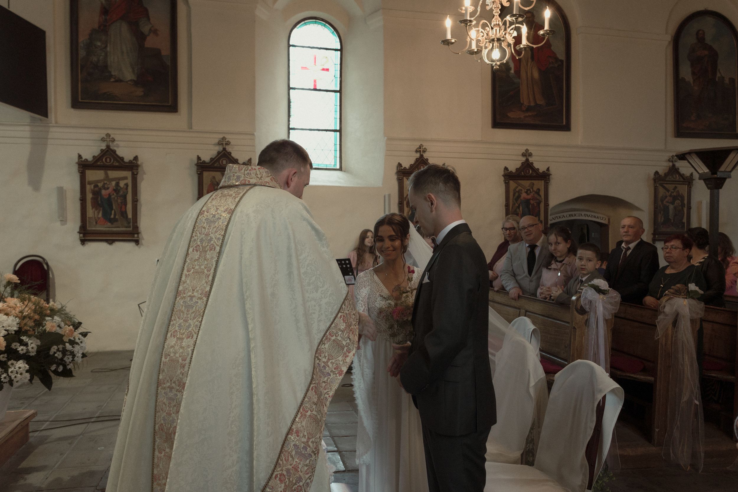 Wedding ceremony taking place in an elegant church with white decor and chandelier.