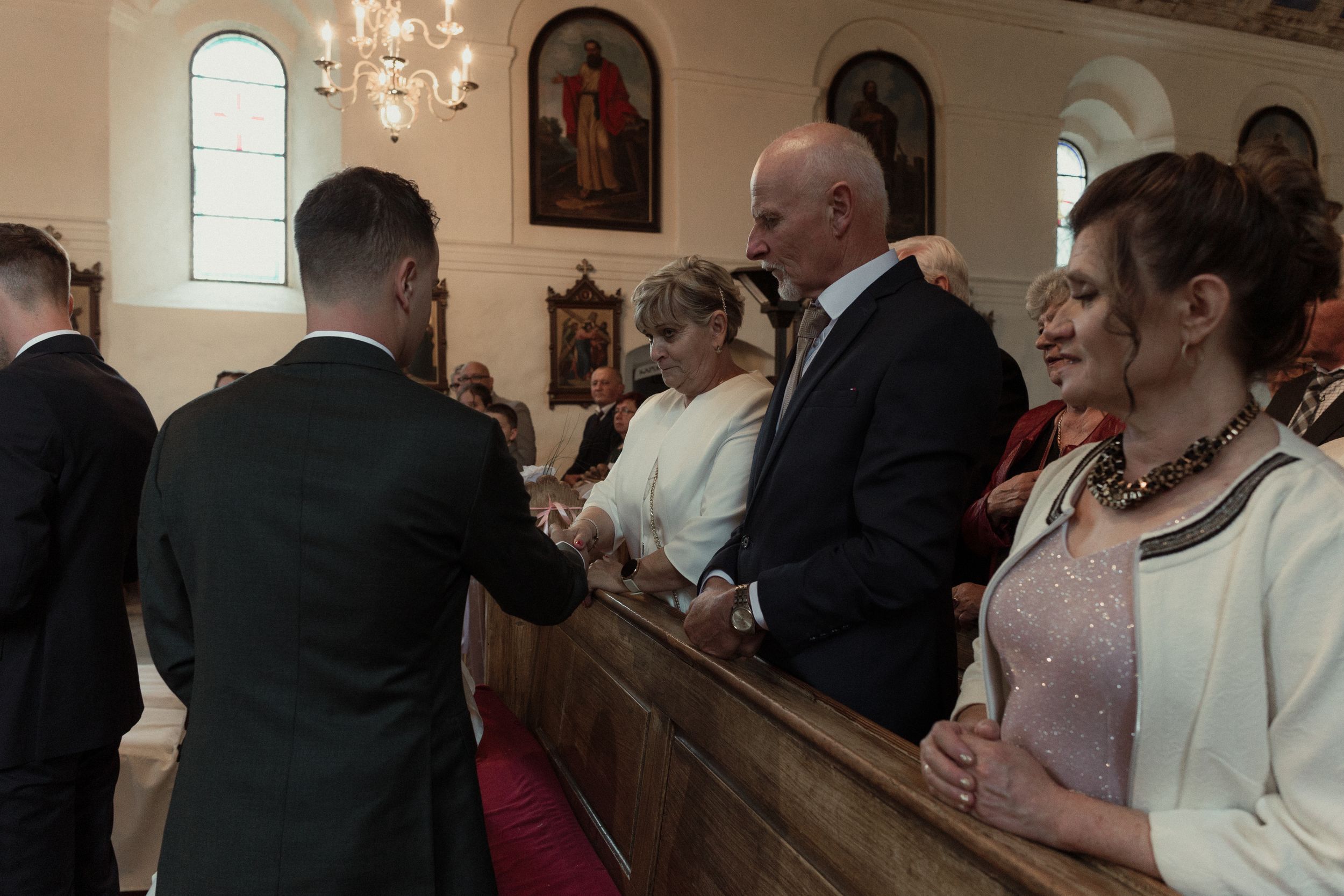 Wedding guests seated in church pews look back at the entrance of an ornate religious ceremony venue.