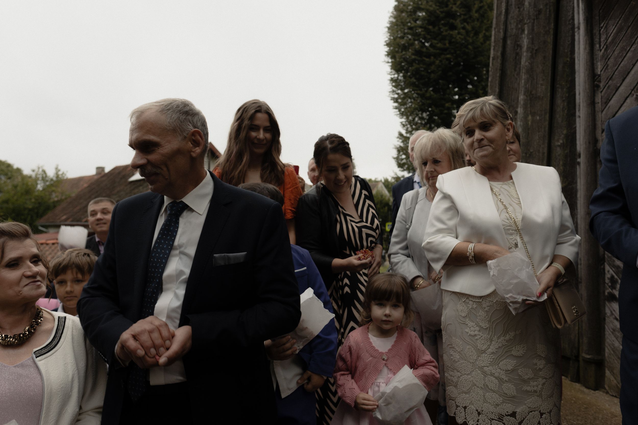 A group of formally dressed people gather outside what appears to be a church on an overcast day.
