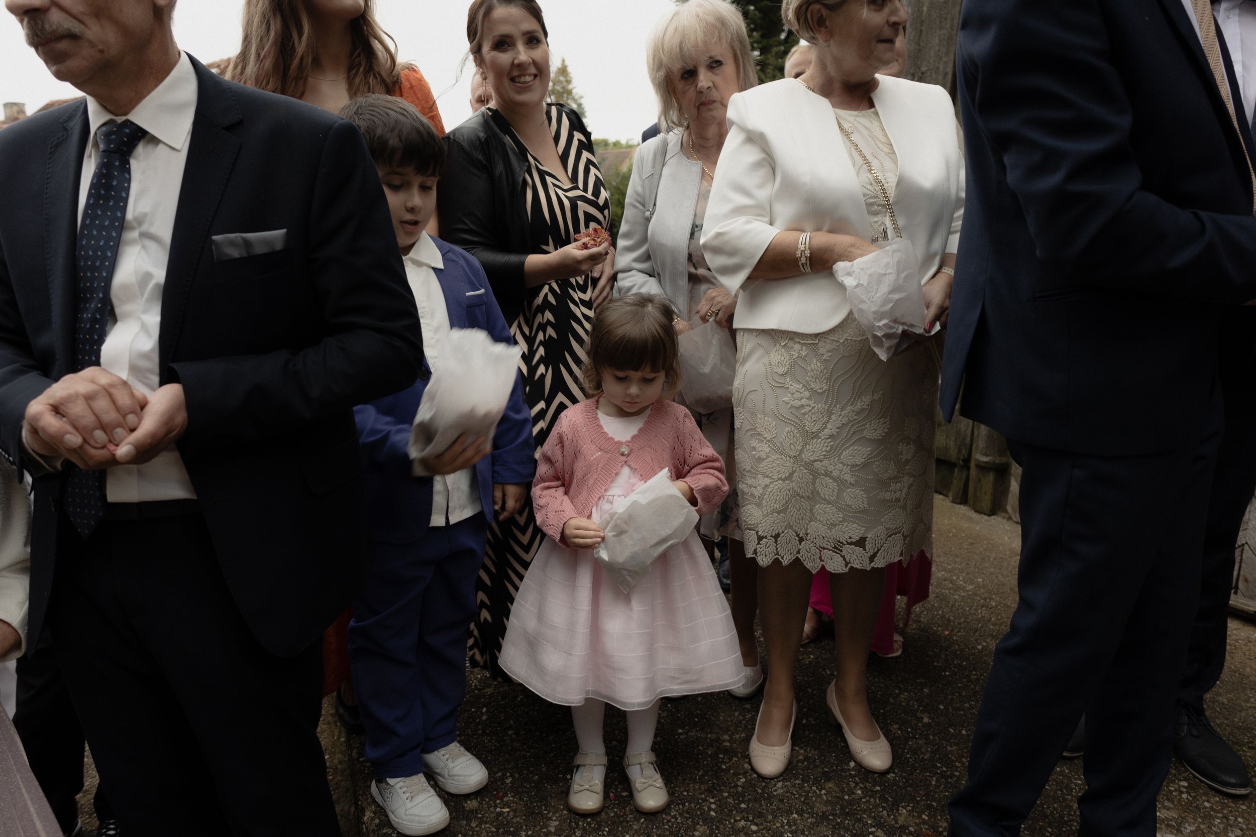 Wedding party guests in formal attire stand and mingle during a social gathering at an outdoor venue.