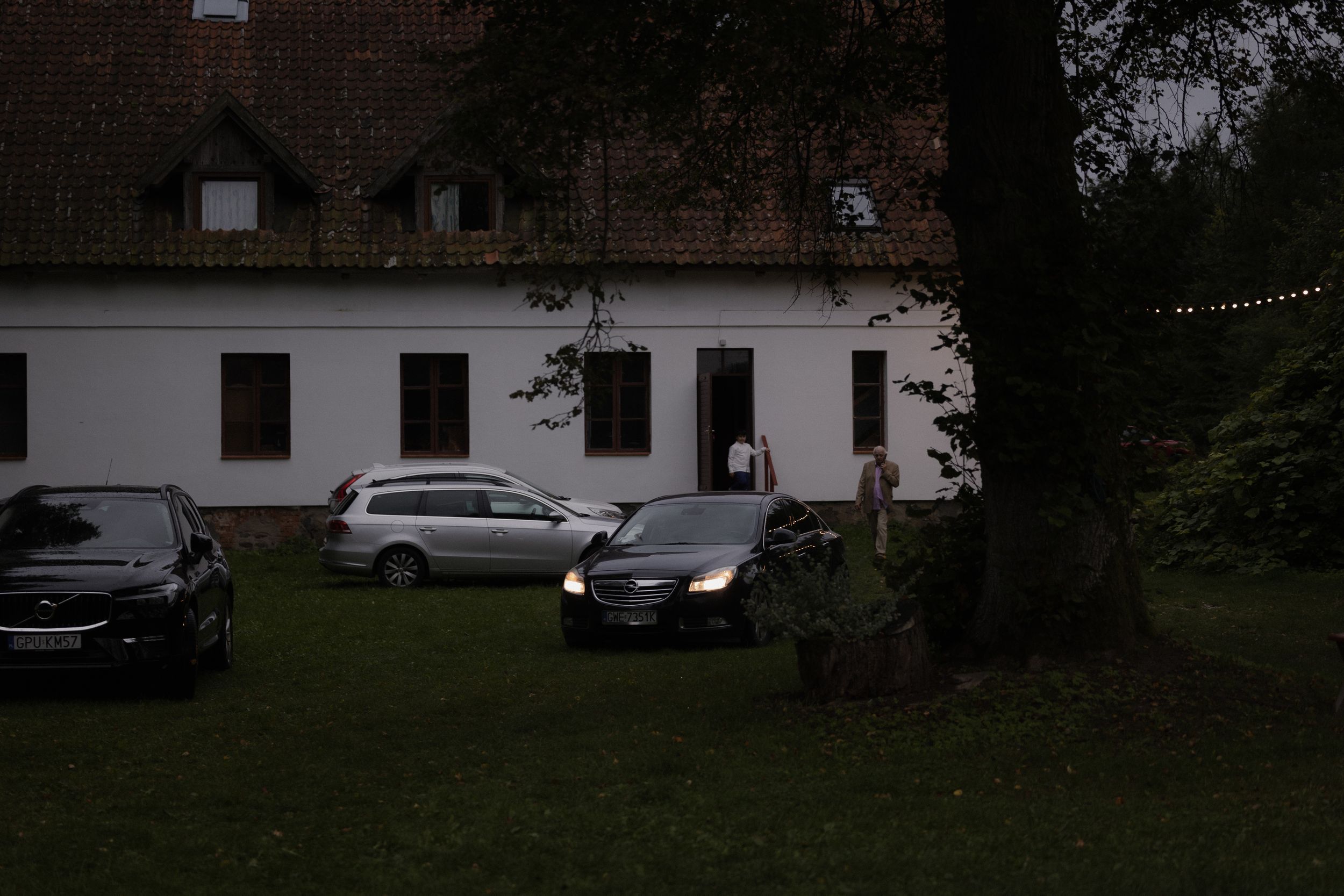 Dark residential neighborhood street at night with parked cars and house lights visible in the background.