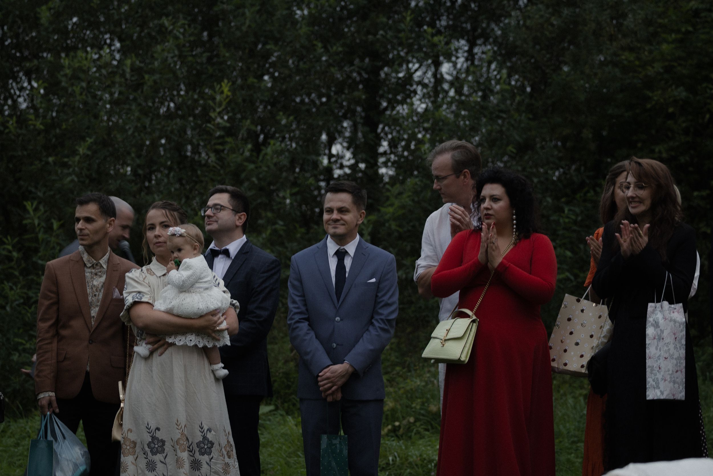 A group of wedding guests pose together in an outdoor garden setting during a formal celebration.