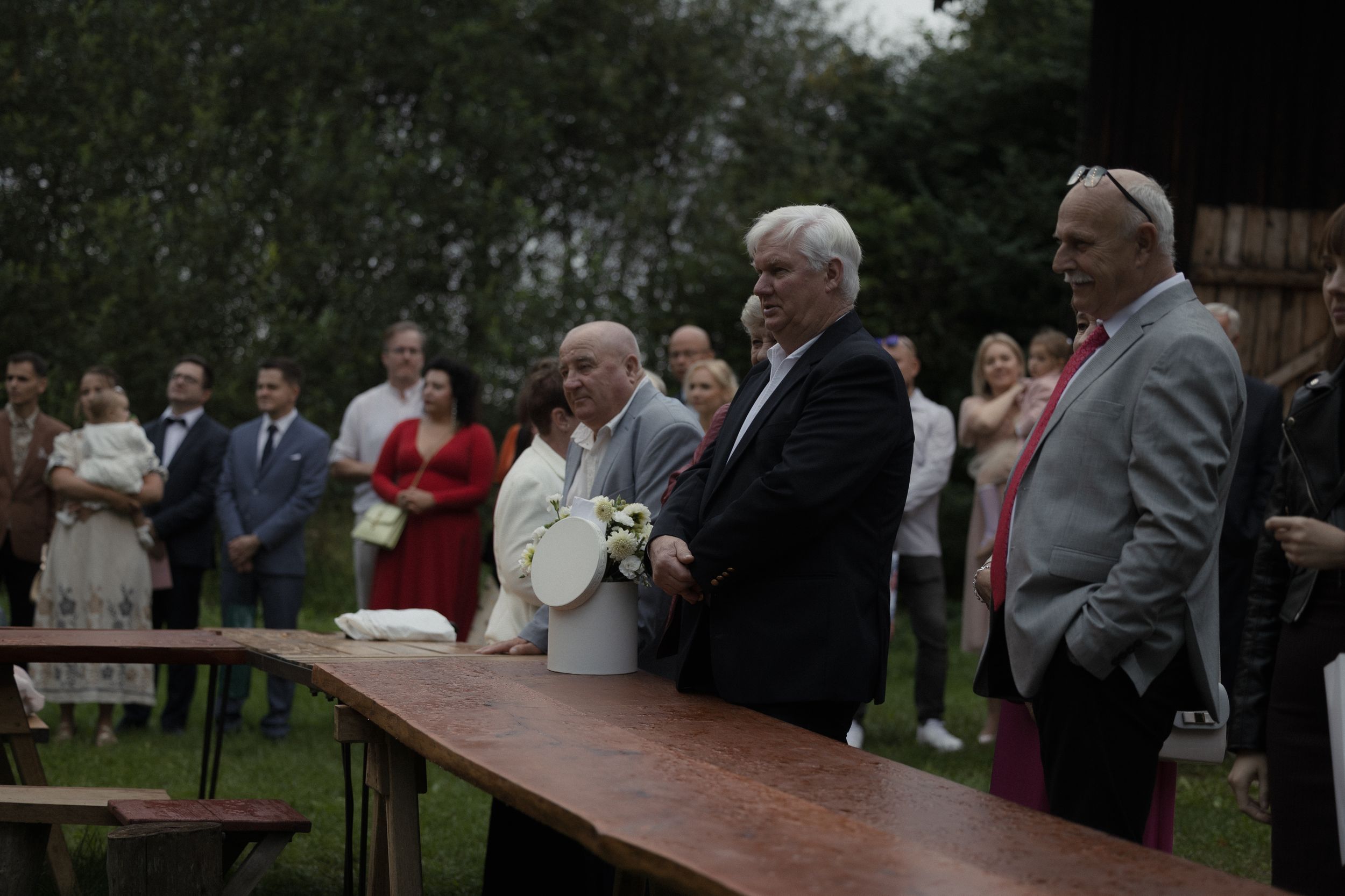 A group of people standing at a long wooden table during an outdoor gathering event.