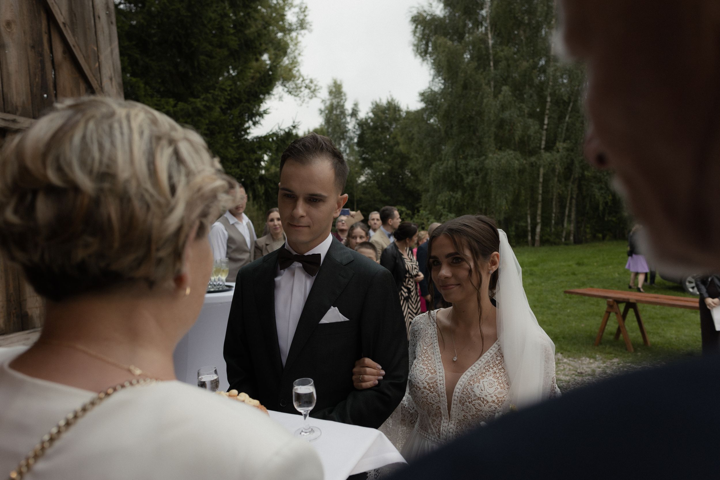 Wedding guests mingle outdoors during a reception in a natural wooded setting.