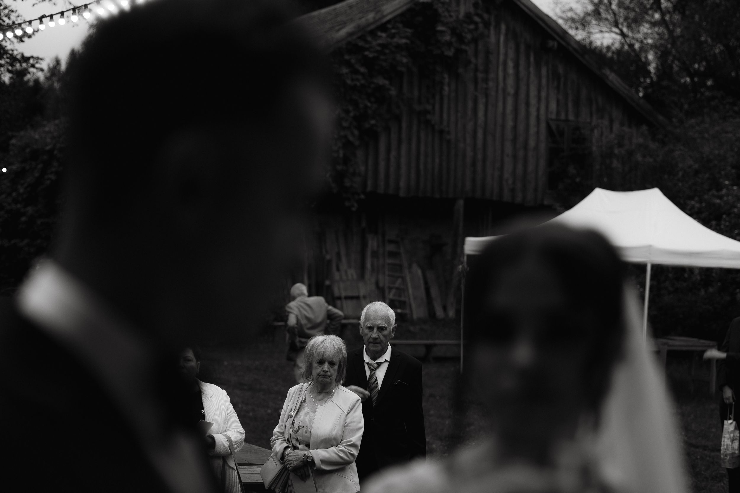 A black and white candid moment during an outdoor wedding reception with guests gathered under a tent.