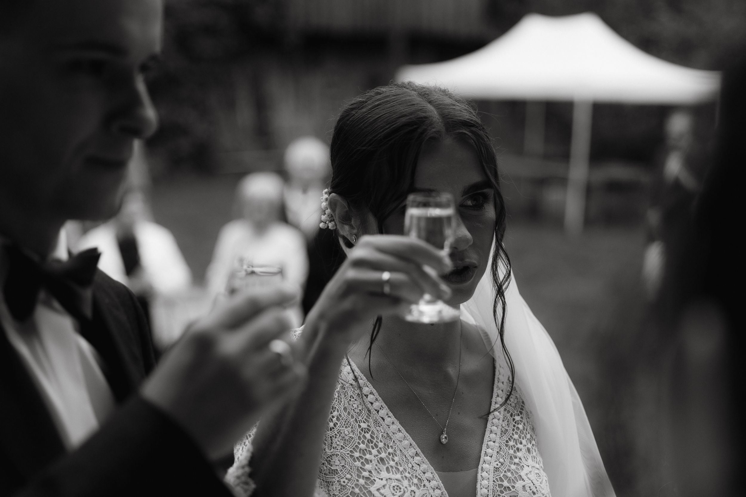 Elegant wedding reception guests mingle and socialize outdoors under a white canopy tent.