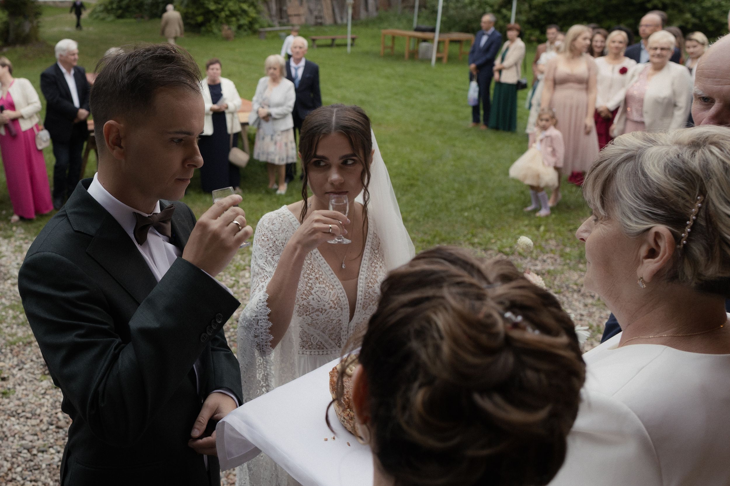 Wedding party and guests share laughter and conversation on a sunny lawn during an outdoor celebration.