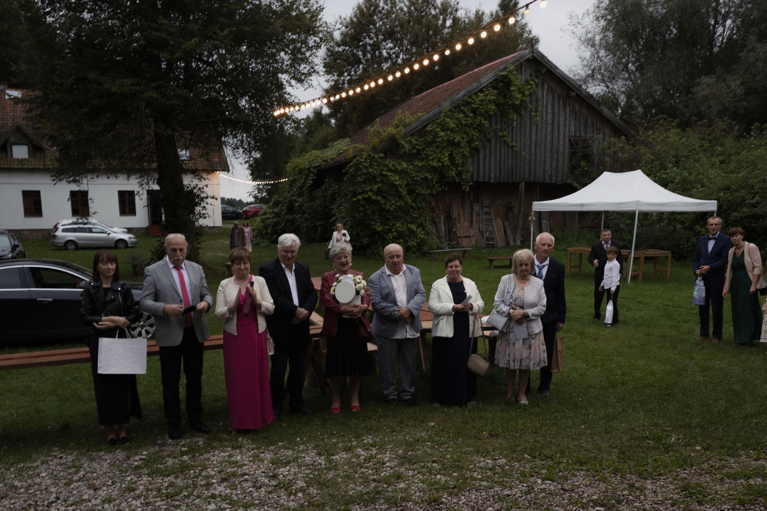 Group of people gathering outdoors at a casual event near trees and tents.