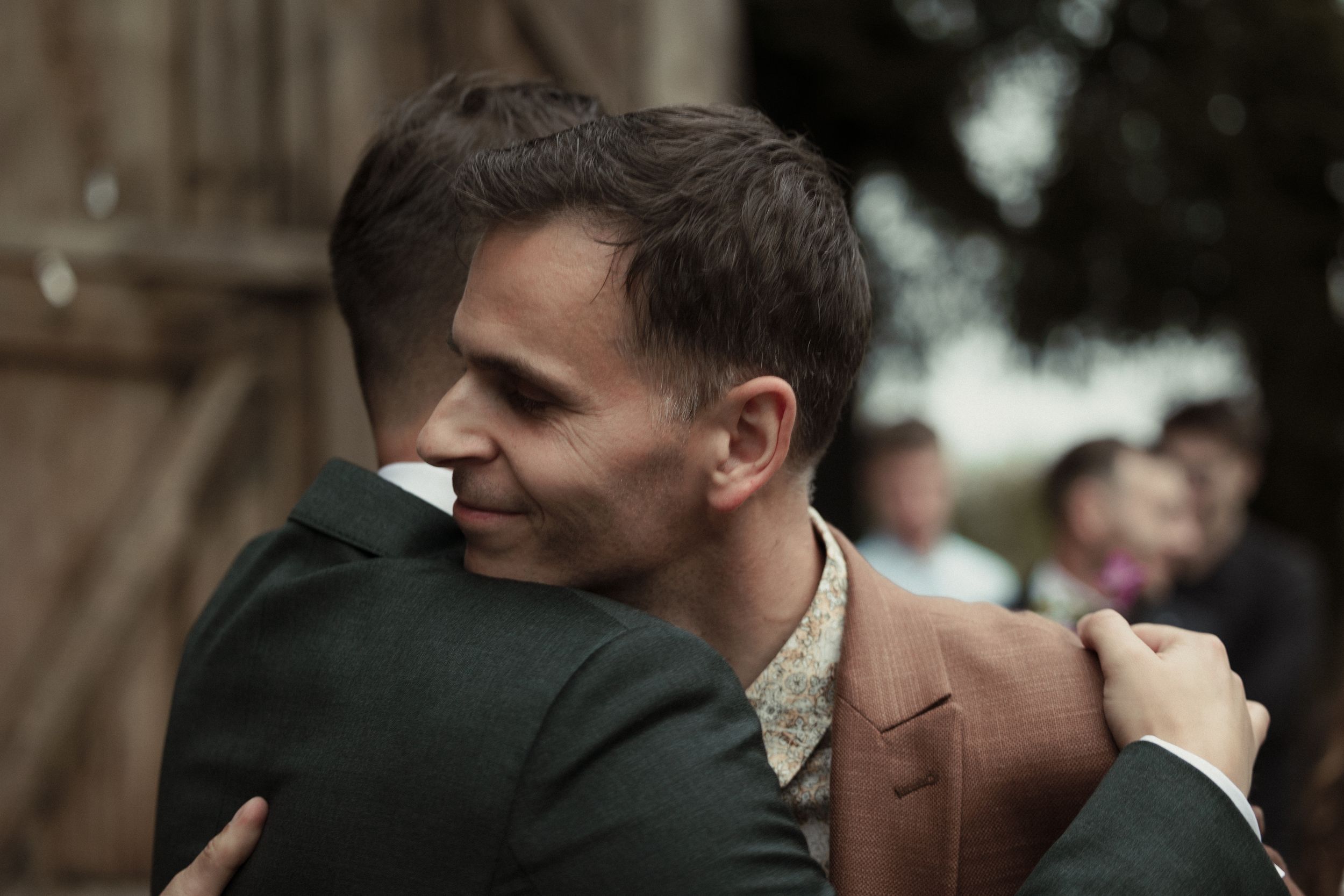 A group of wedding guests gather outside, laughing and smiling during a joyful outdoor celebration.