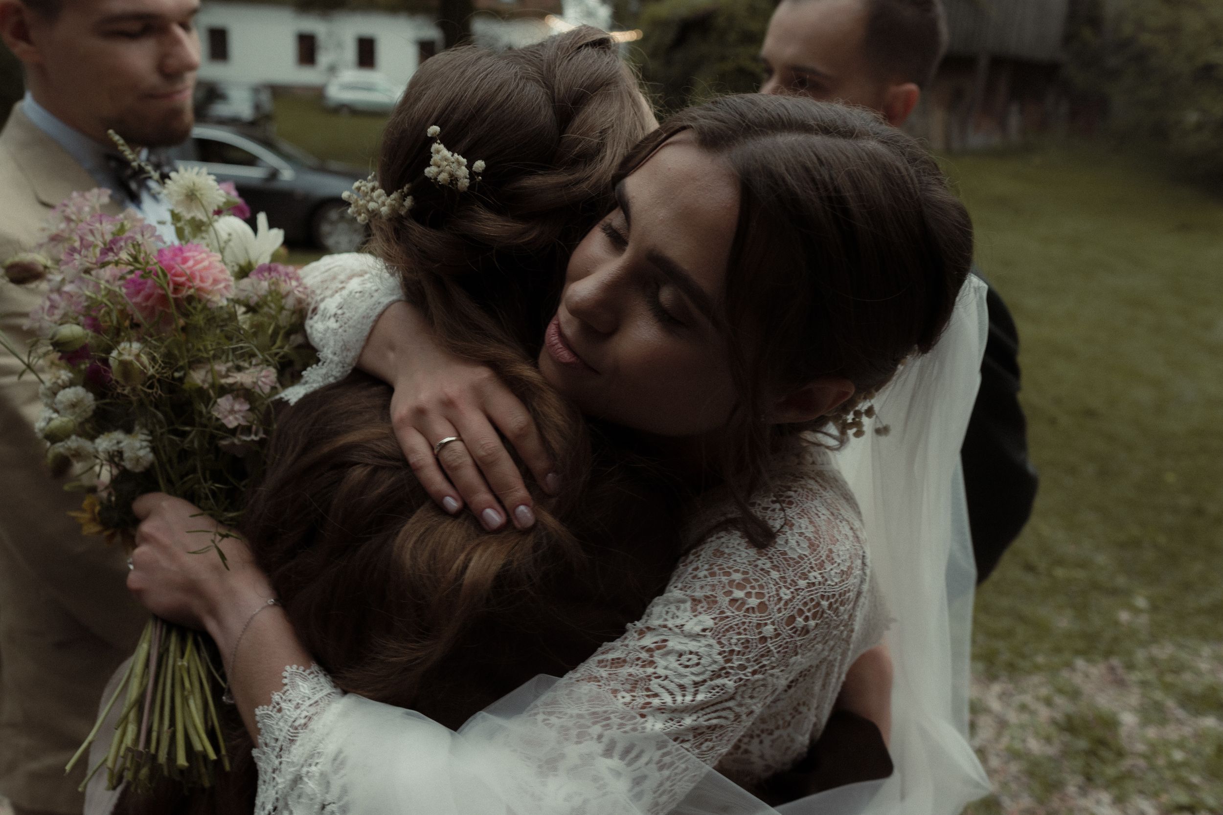 Close-up portrait of a wedding couple sharing a tender kiss while holding a vibrant floral bouquet outdoors.