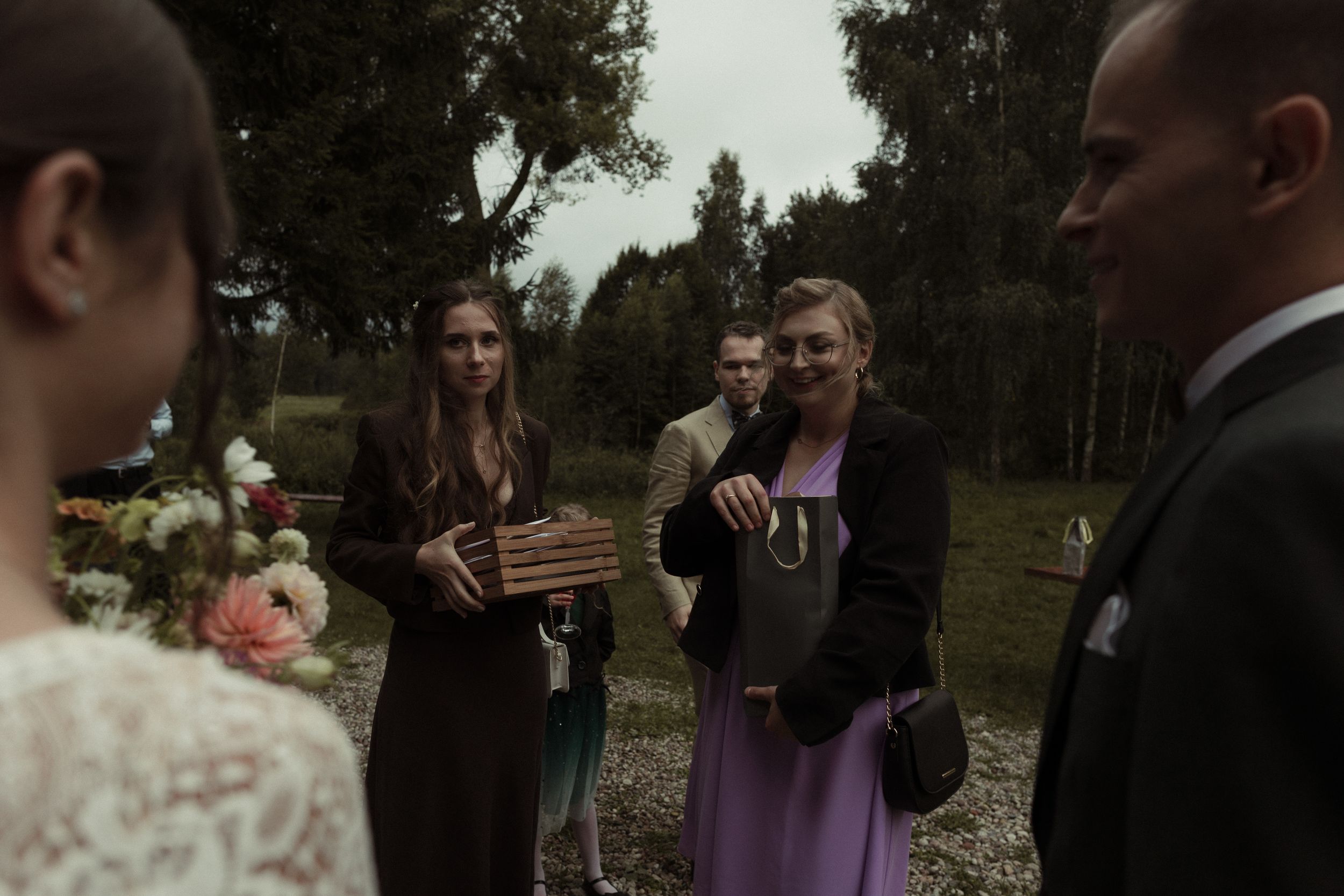 A crowd gathers outdoors celebrating at what appears to be a wedding ceremony in a natural setting.