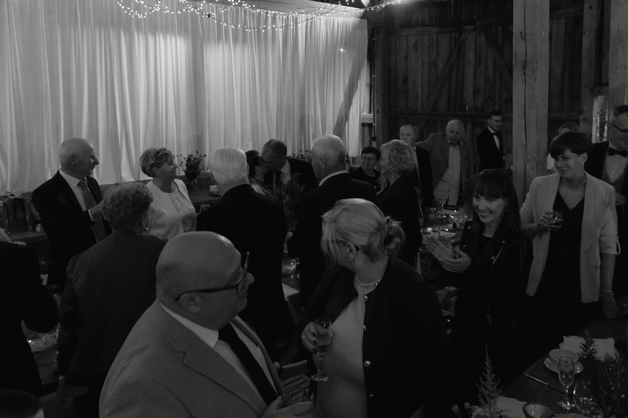 A black and white photograph of a crowded social gathering with people mingling in a room with curtained windows.