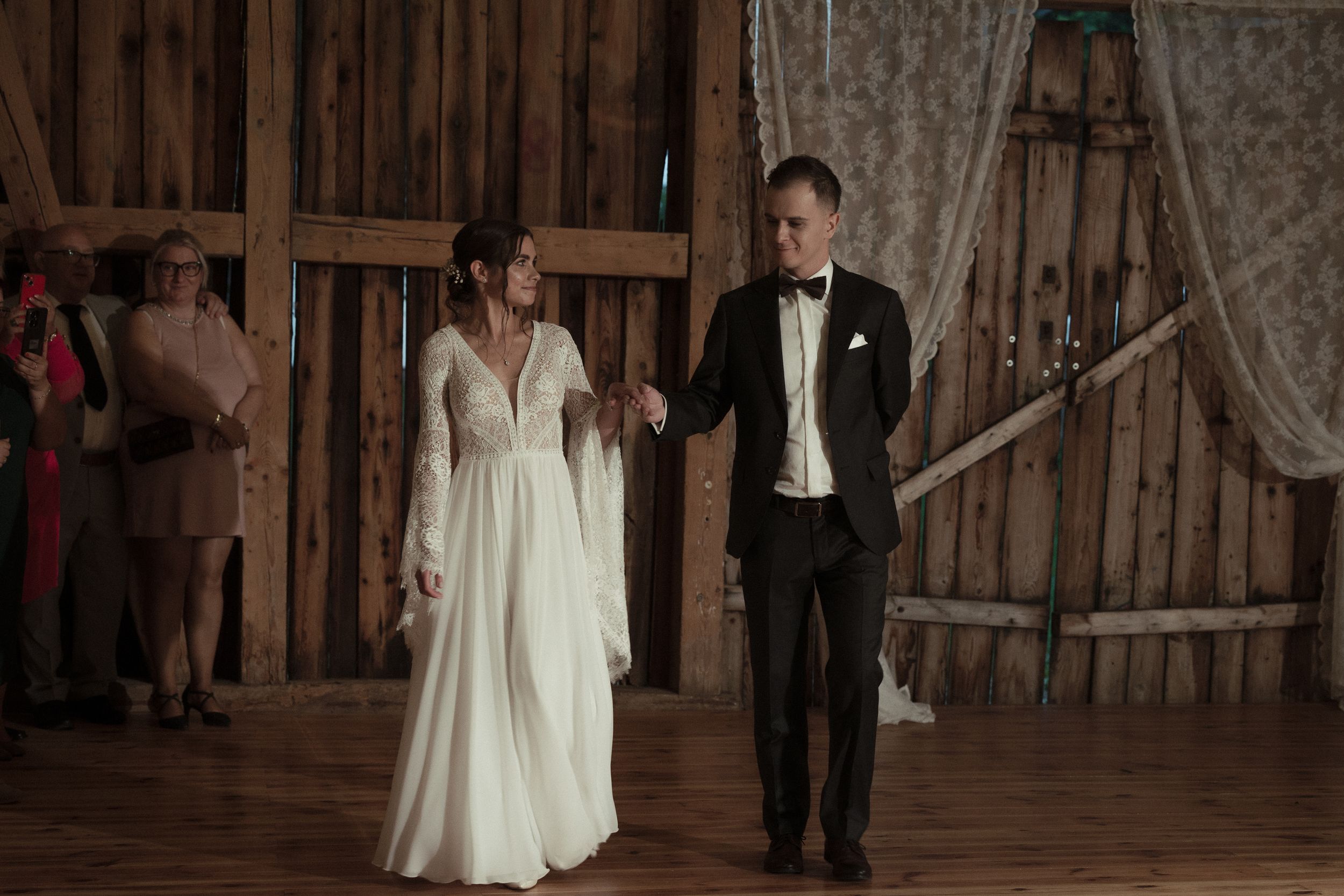 A bride and groom walk together through a rustic wooden barn during their wedding celebration.