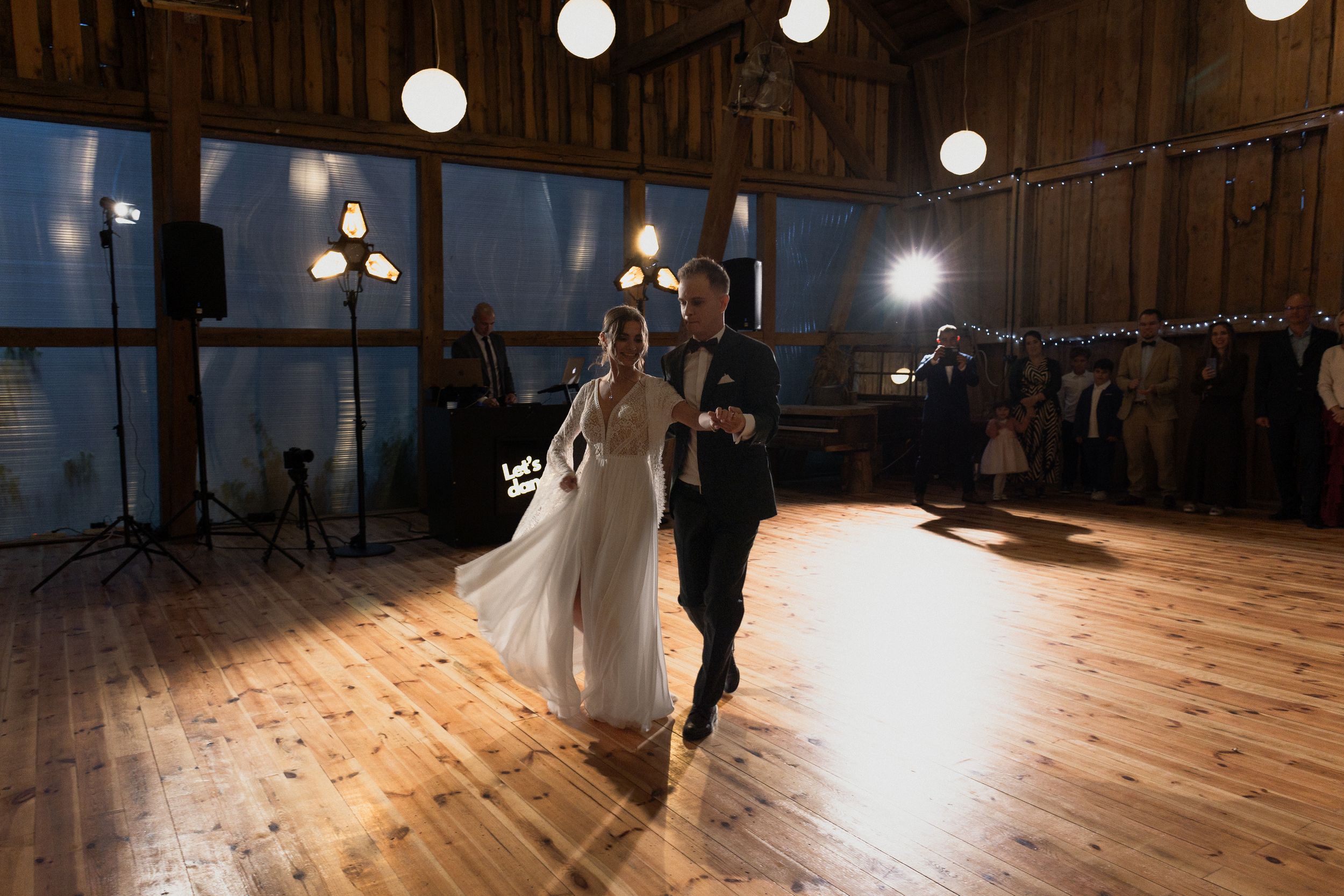 A large empty dance hall with wooden floors, string lights overhead, and dramatic lighting creating moods and shadows.