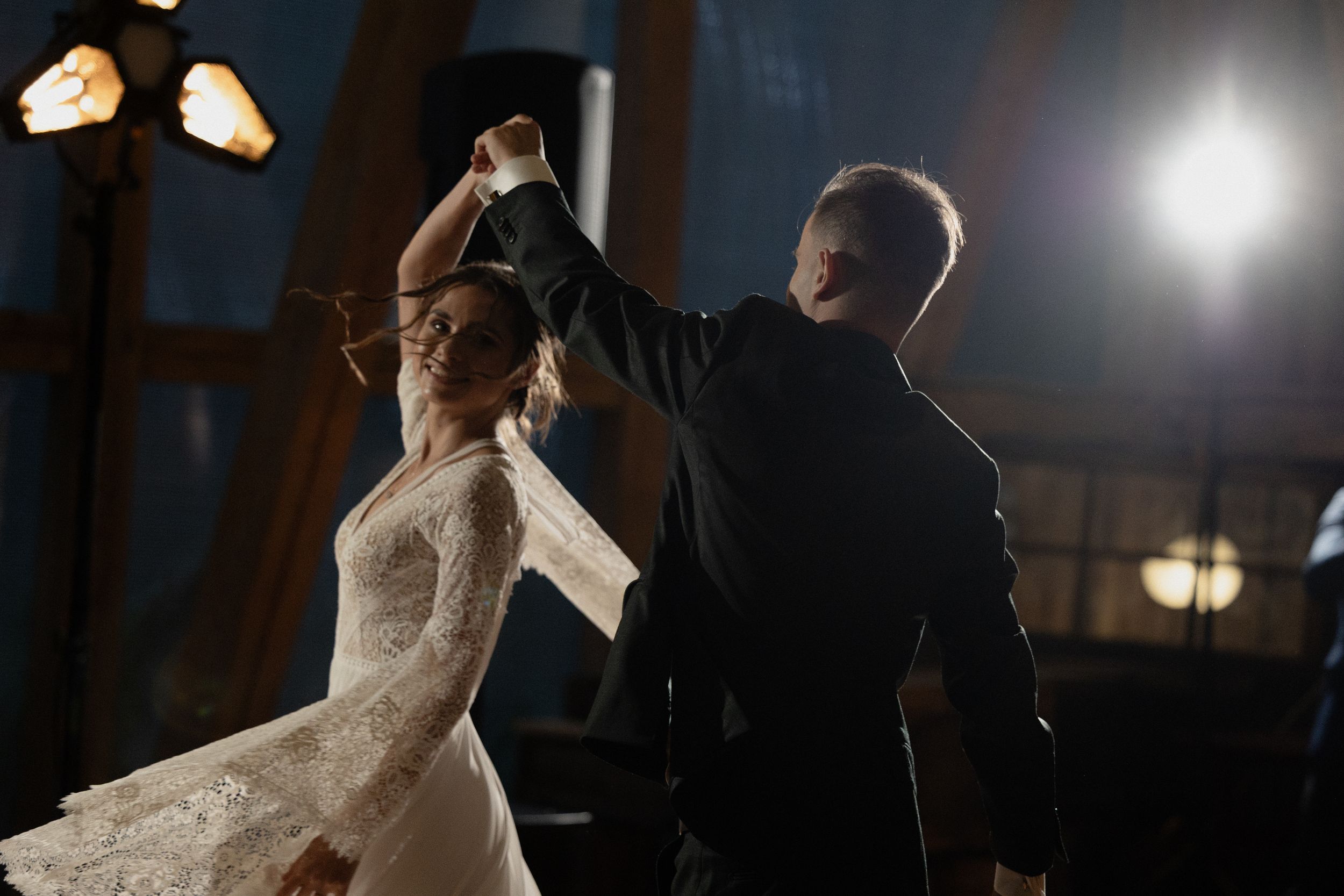 A couple dances elegantly at night, with the bride's lace dress flowing as her partner leads in a dramatic dance move.