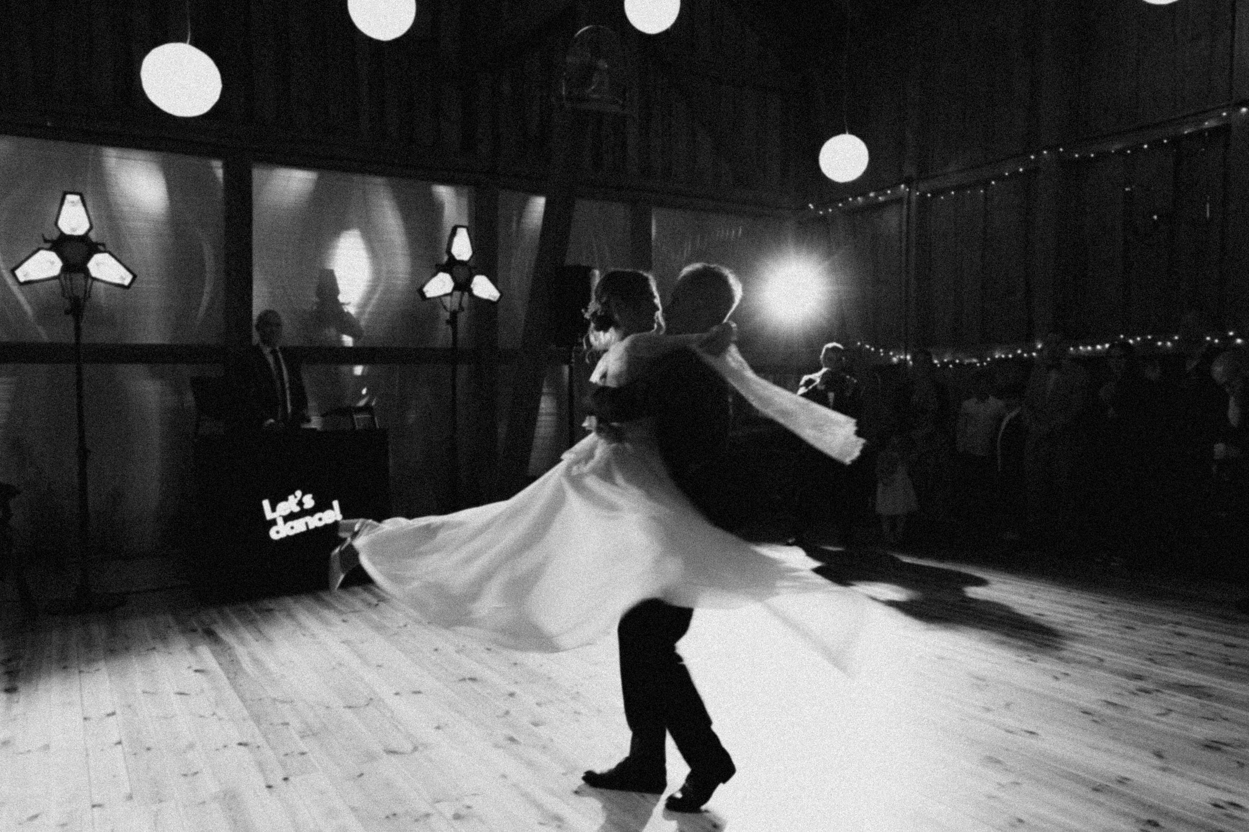 Dancers in silhouette perform elegant ballroom dance moves on an illuminated dance floor beneath glowing lights.