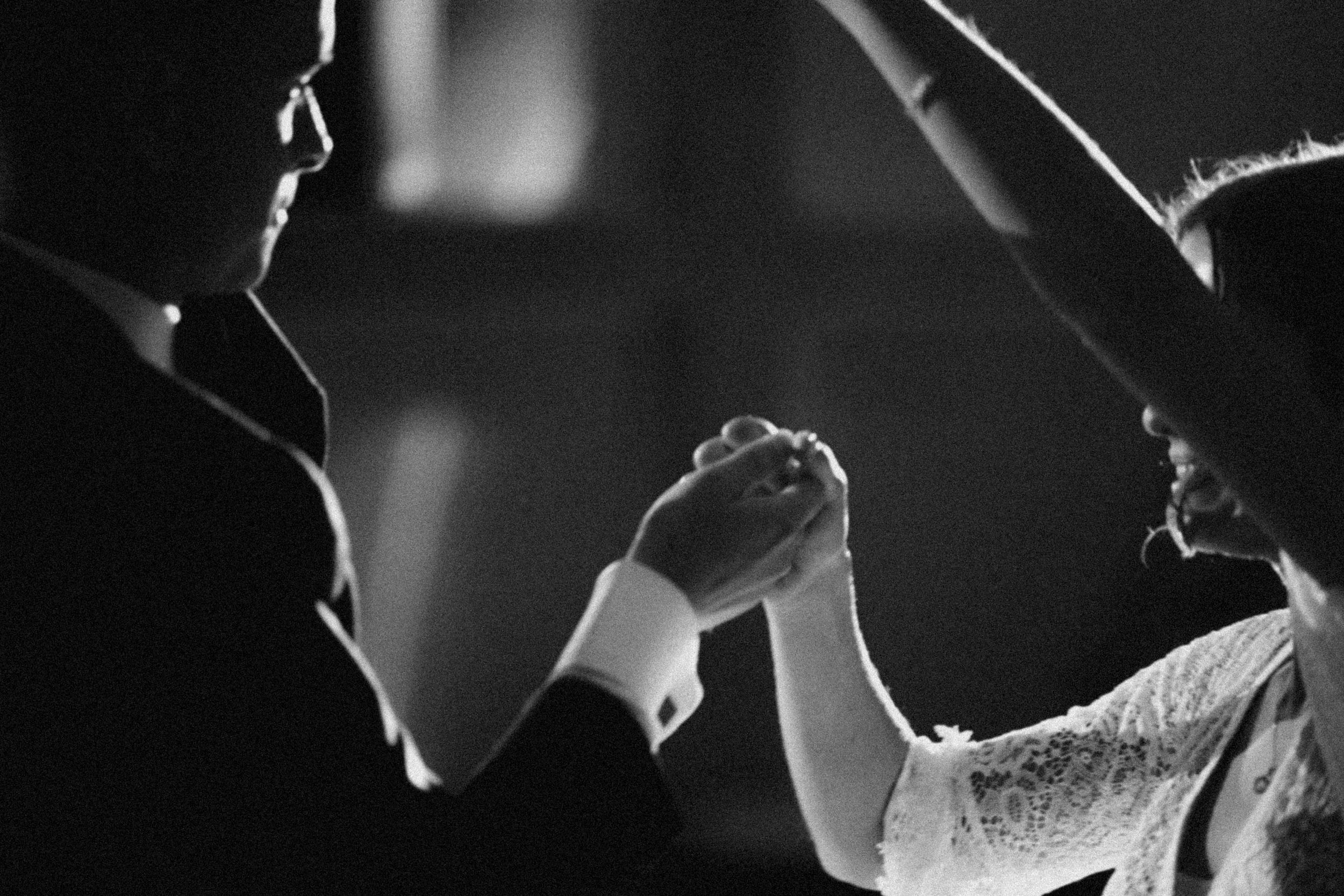 A romantic silhouette of a couple holding hands and dancing together in black and white.