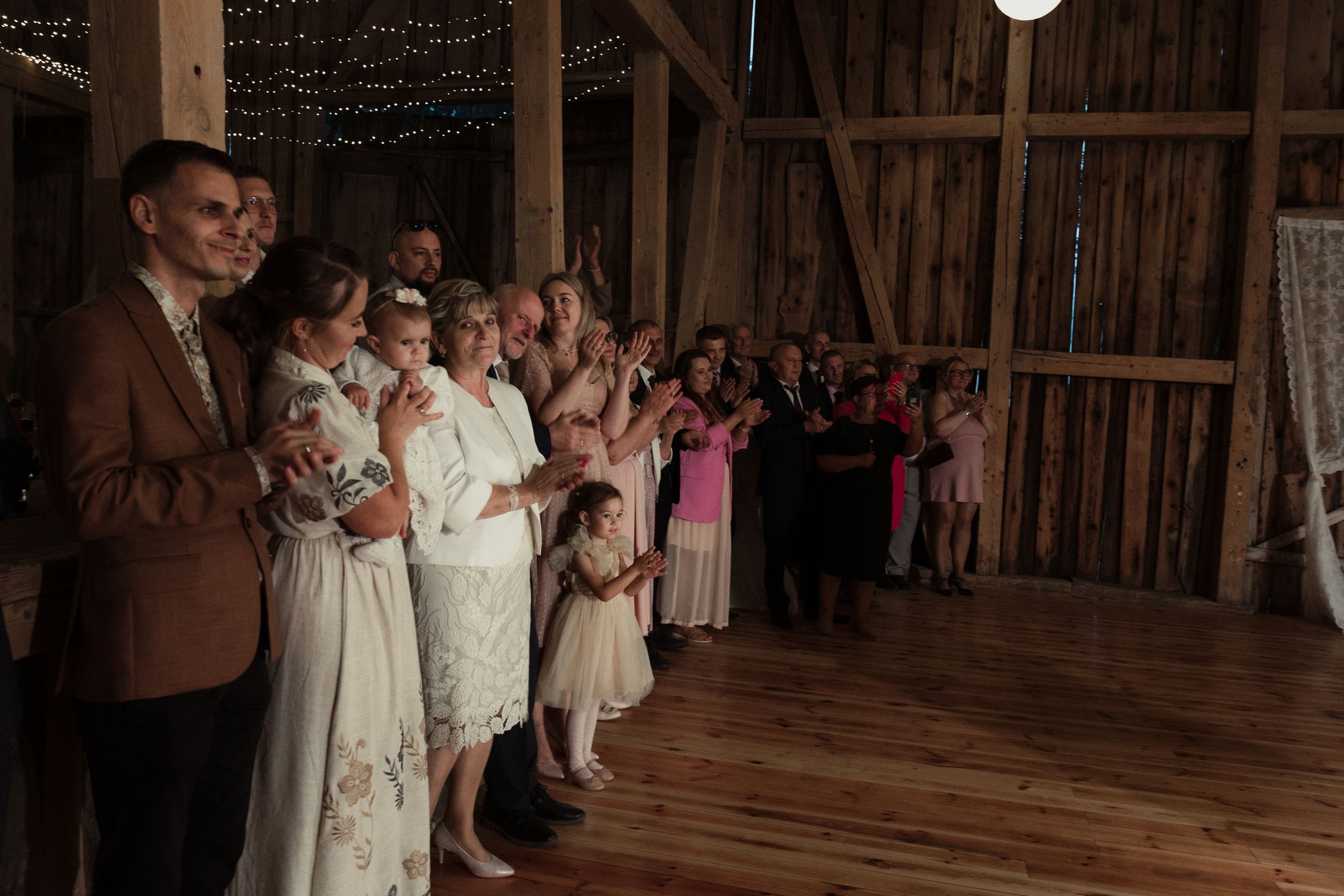 Wedding guests gather together in a rustic wooden barn venue decorated with string lights.