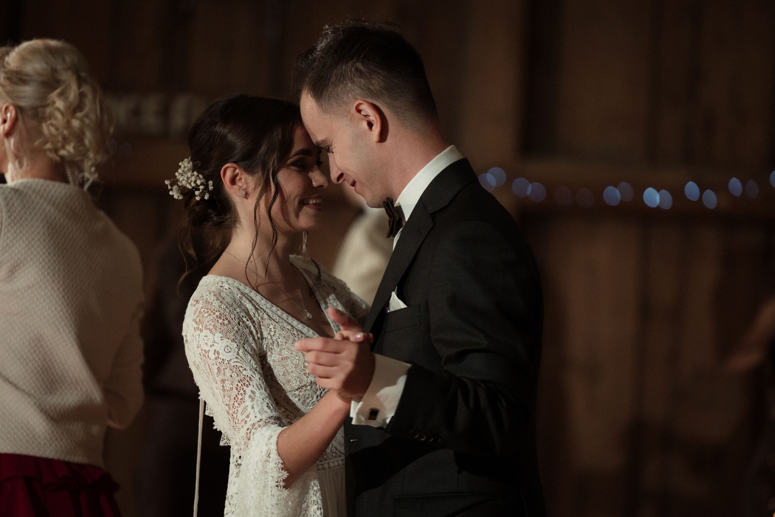 Newlywed couple gazes lovingly at each other during first dance in dimly lit ballroom setting.