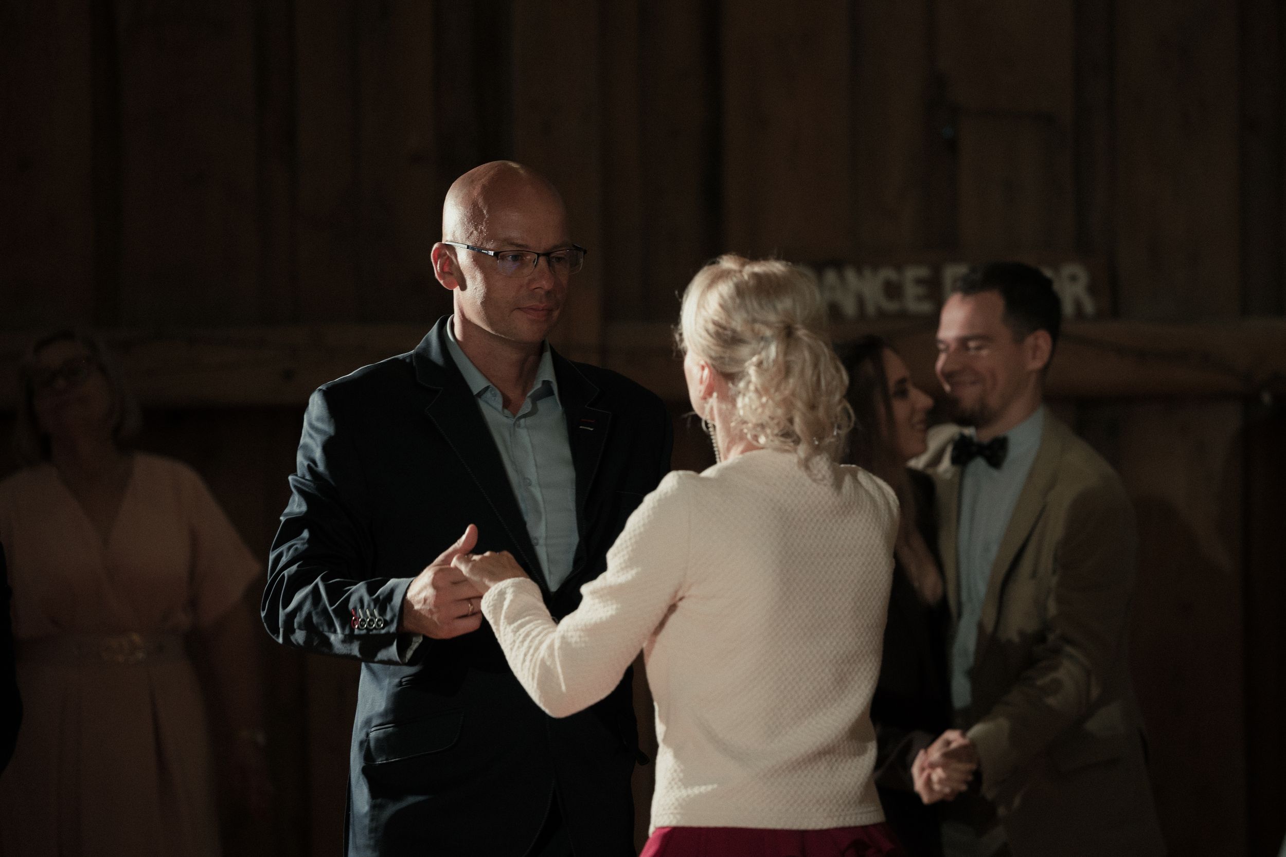 A group of people dance together on a dimly lit dance floor during an evening celebration.