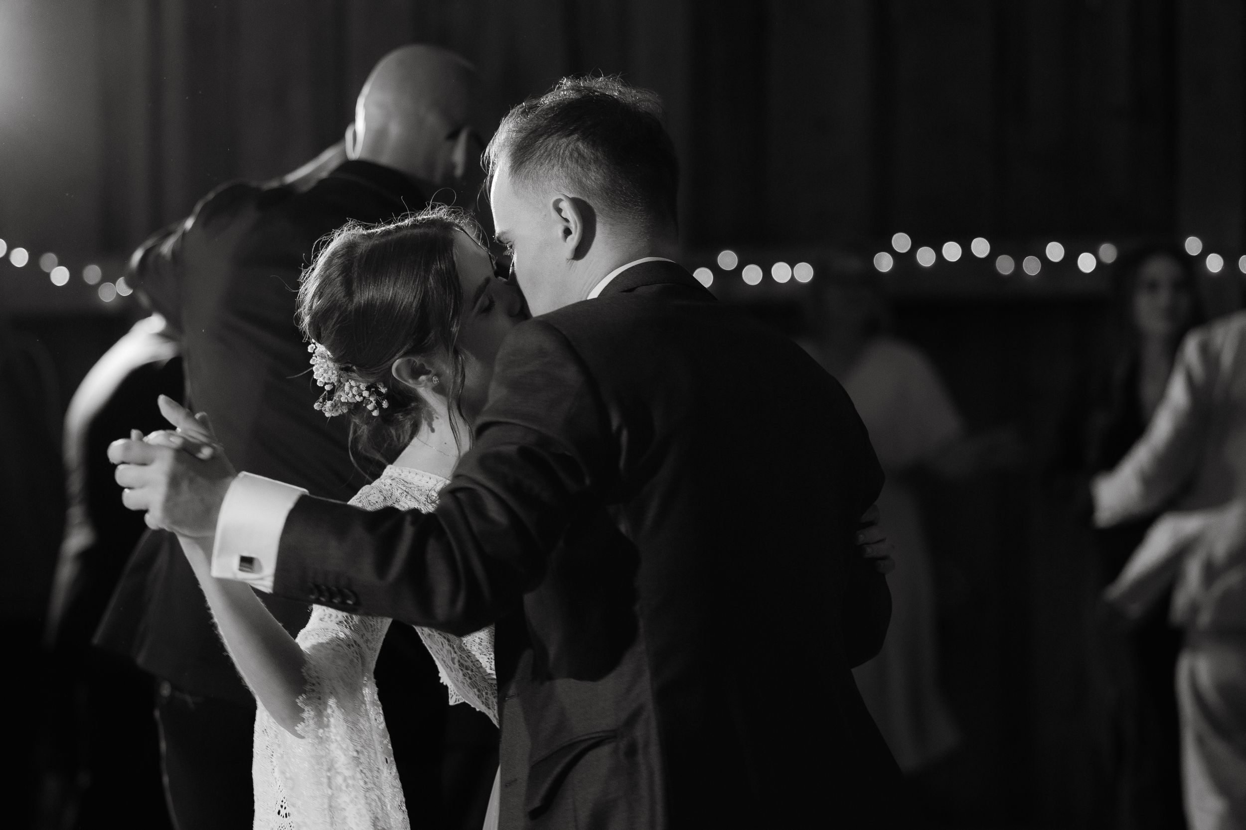 A couple dances together during a wedding reception under twinkly lights.