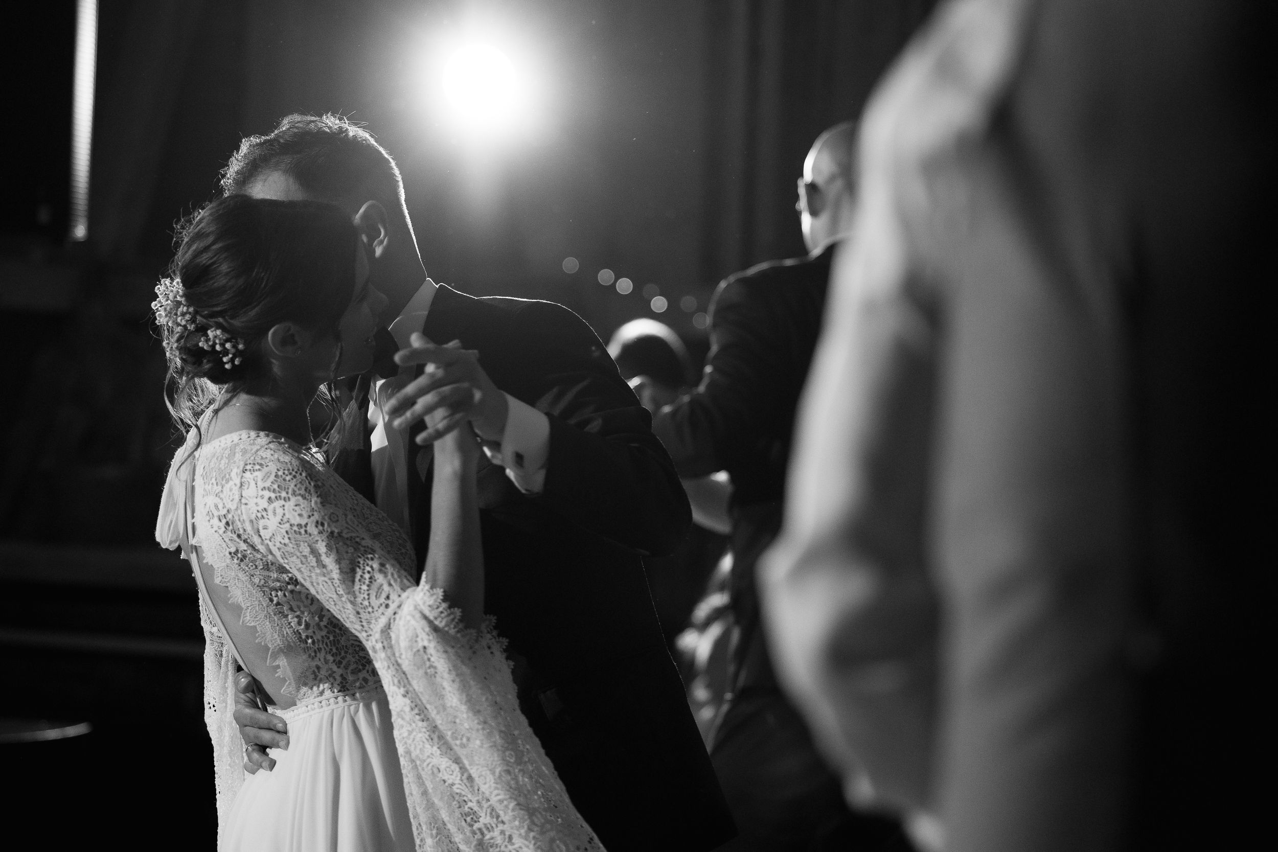 A newlywed couple shares their first dance under dramatic lighting at their wedding reception.