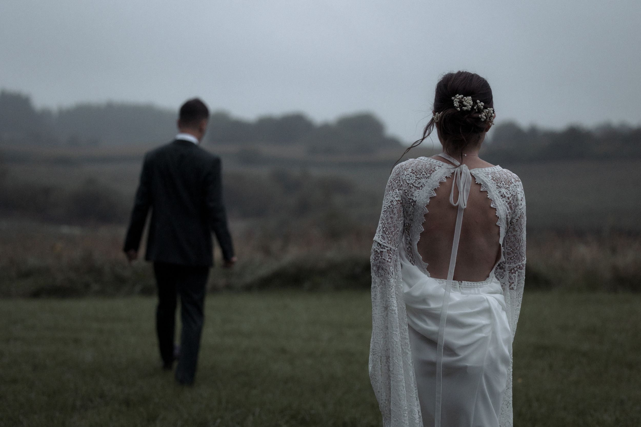 A couple in wedding attire walks together through a misty field on their special day.