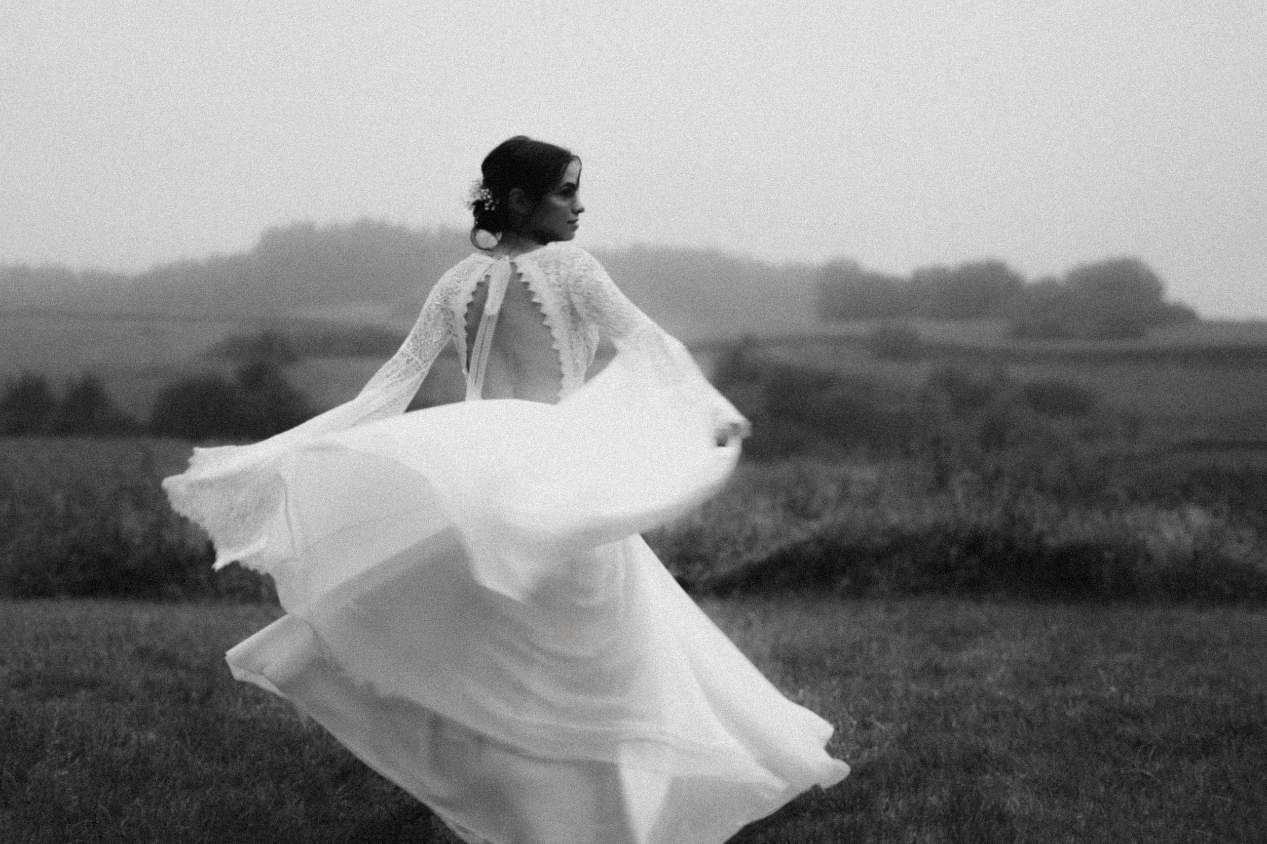 A flowing white dress billows in the wind against a moody landscape in black and white.