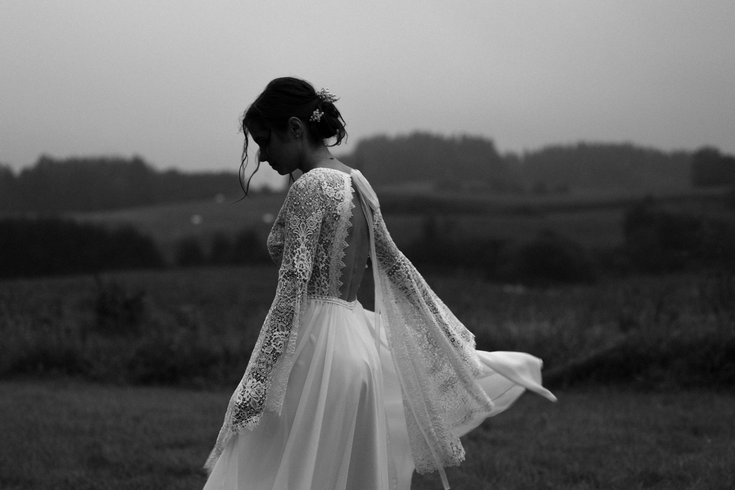 Black and white photo of a romantic couple embracing in a field on their wedding day.