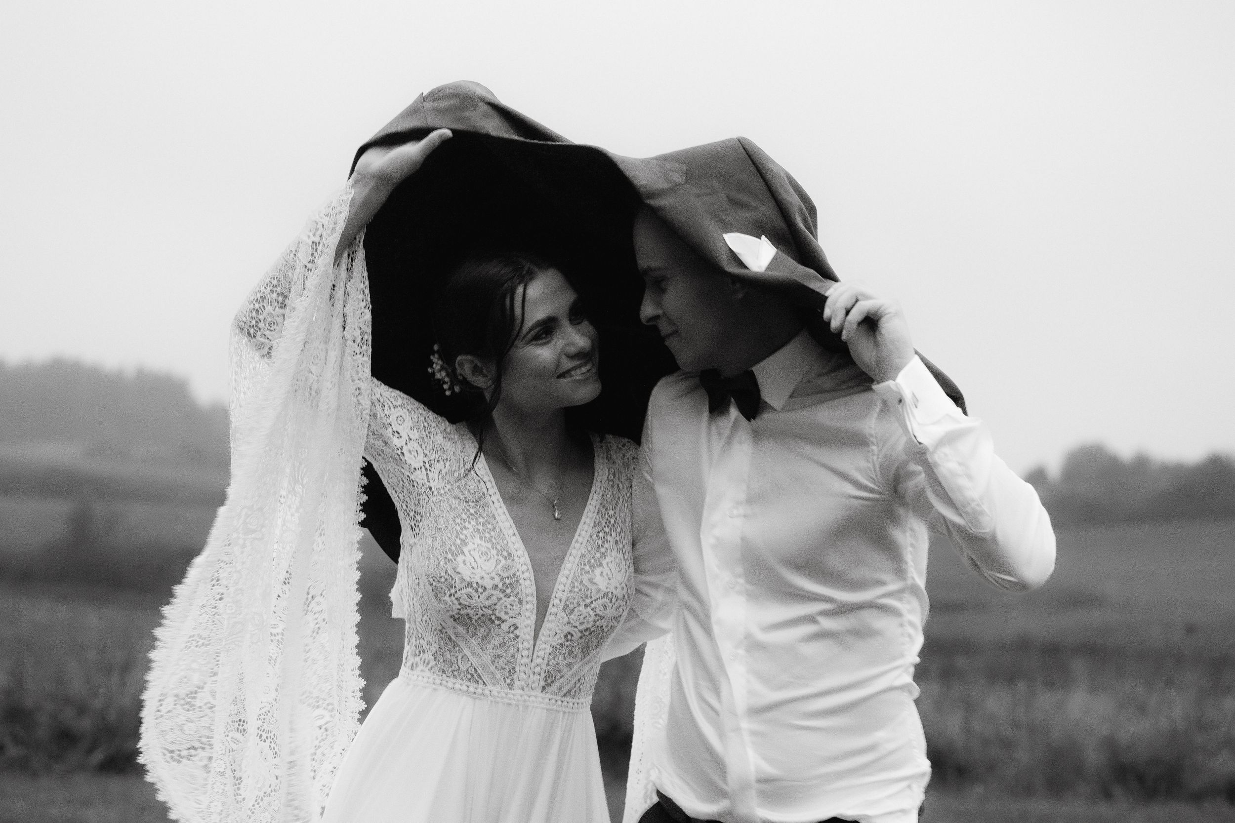 A newlywed couple shares an intimate moment in a rustic outdoor setting, captured in monochrome.