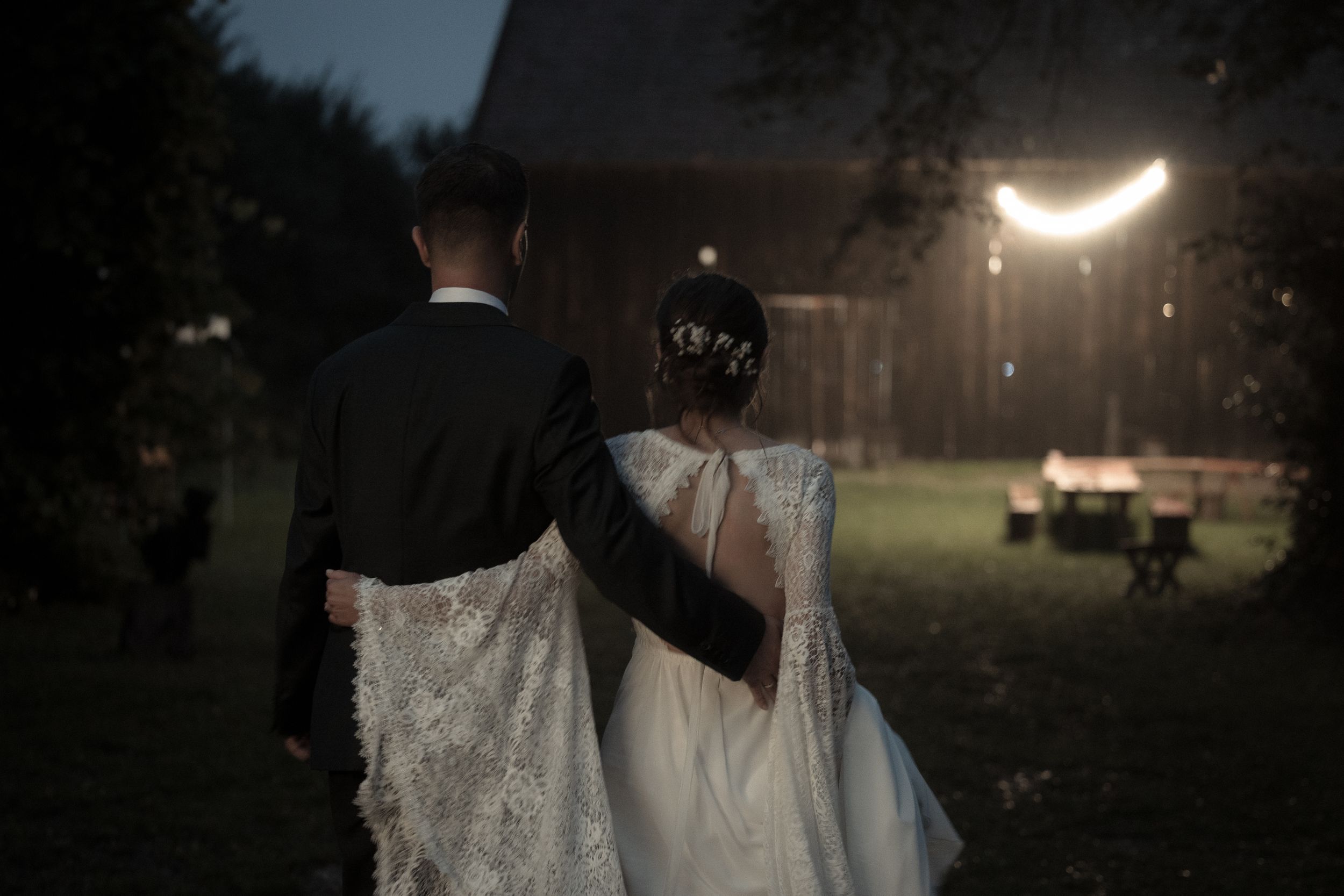 A wedding couple shares a romantic dance outdoors in front of a glowing crescent moon, creating a dreamy atmosphere.