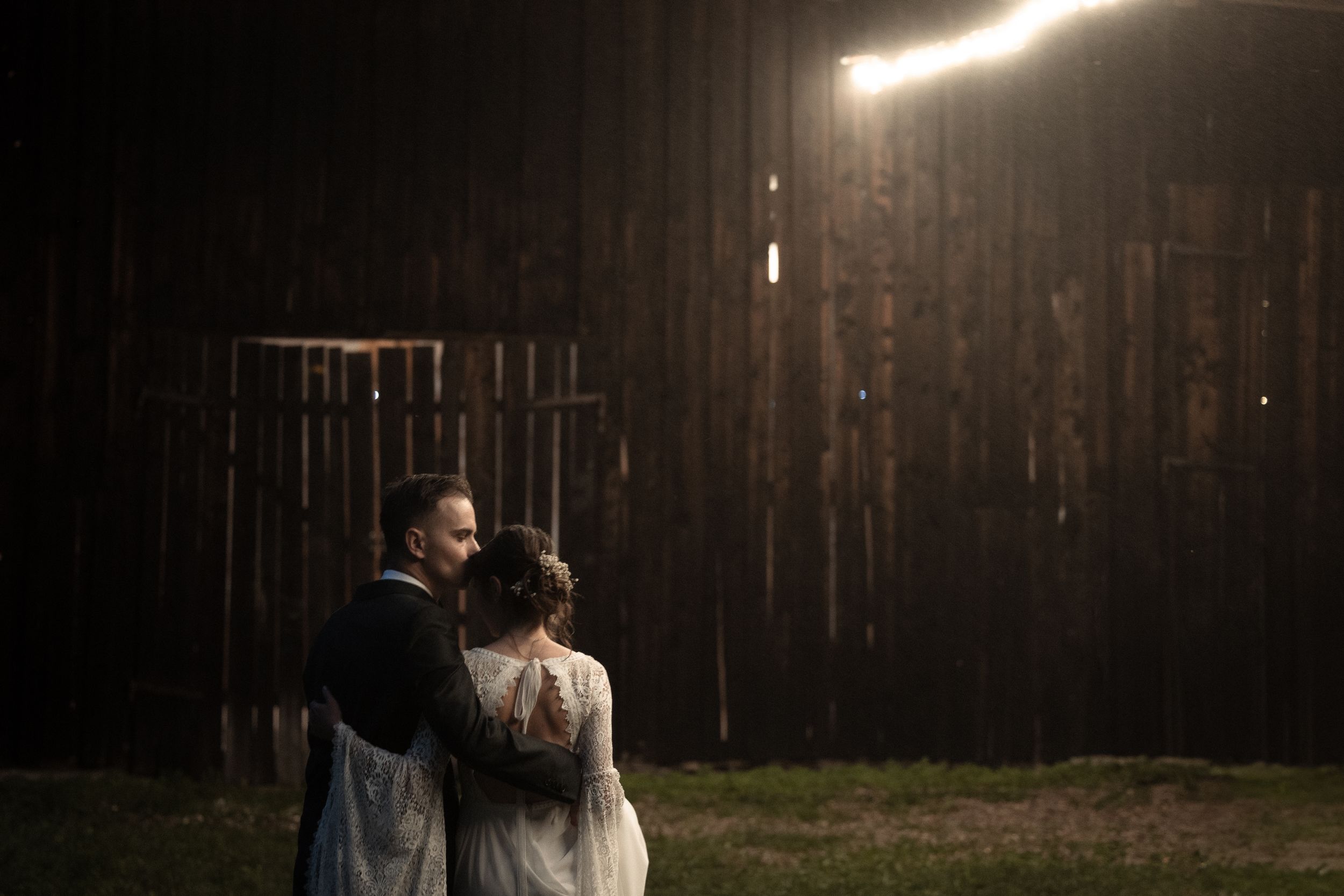 Silhouettes of a romantic couple standing in the rustic wooden barn lit by warm streaming sunlight through slats.