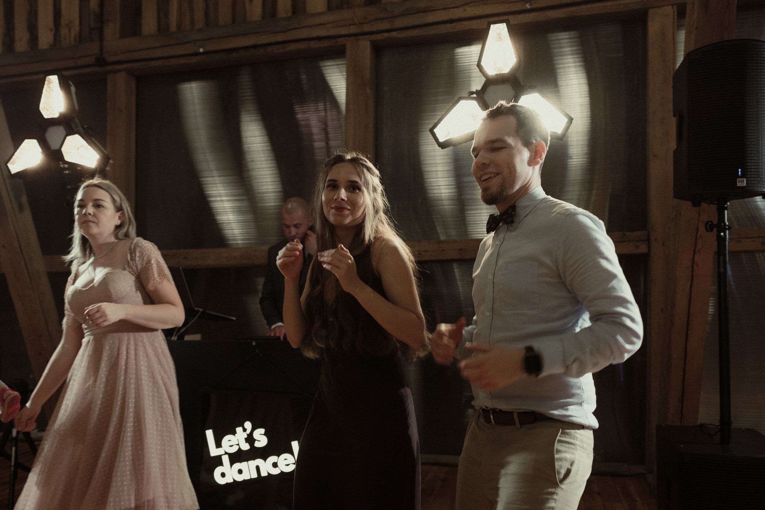 People celebrating at a rustic wedding reception venue with wooden walls and vintage lighting fixtures.