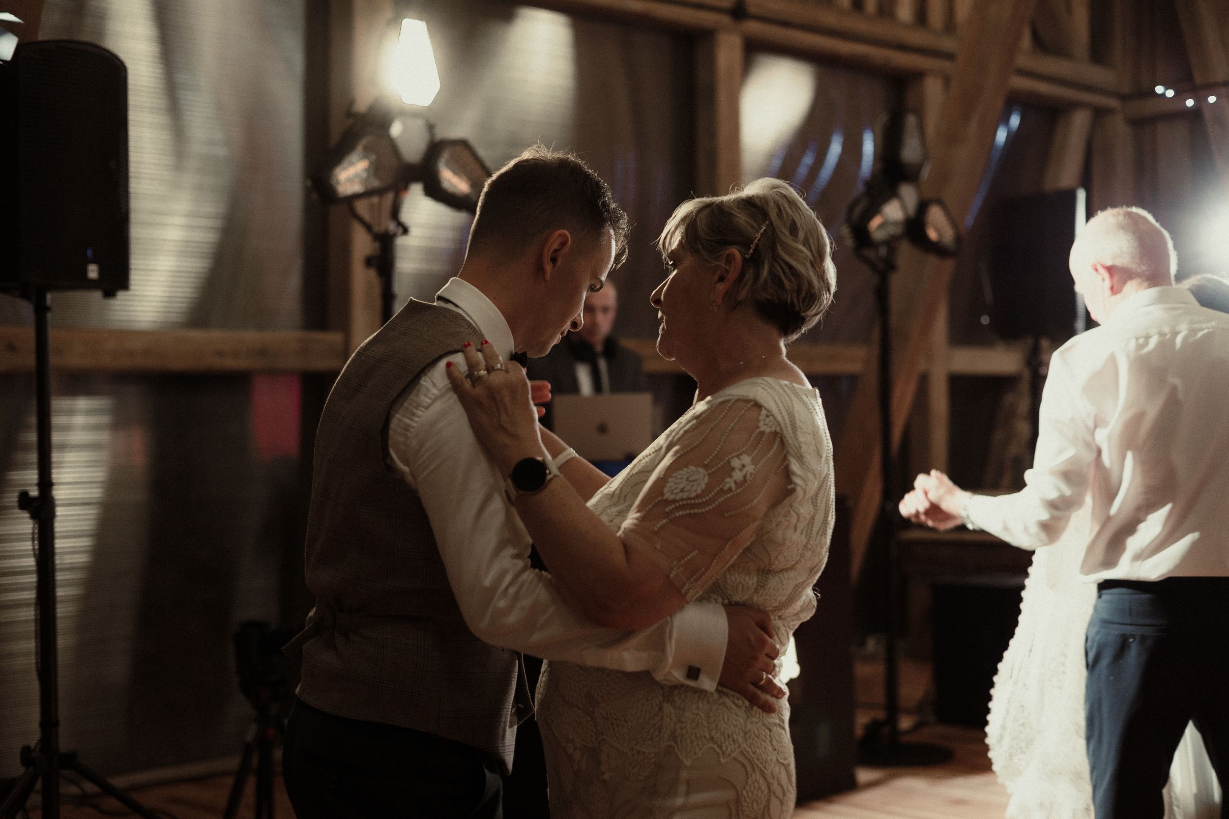 A couple shares their first dance at a rustic barn wedding reception in warm ambient lighting.