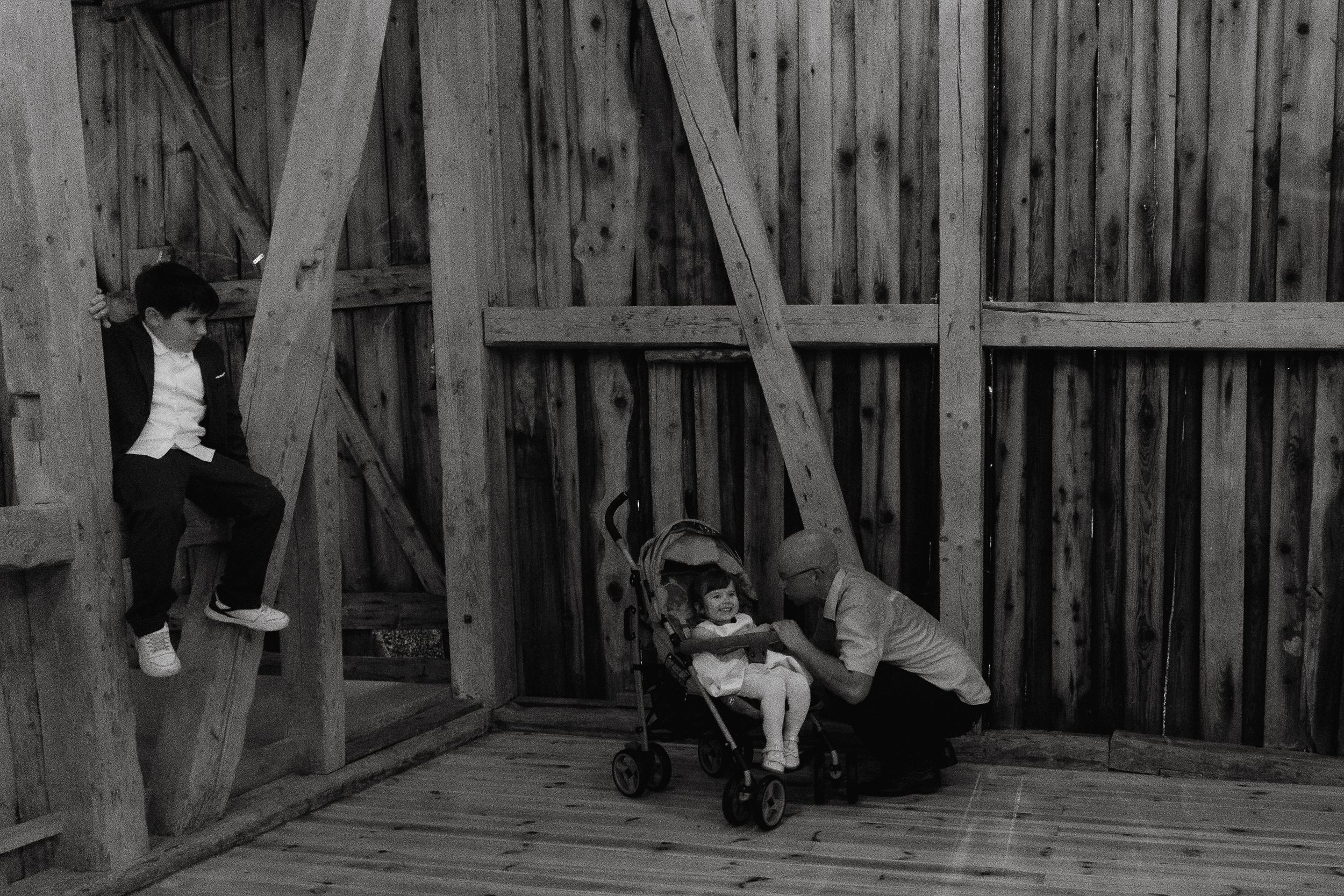 Black and white photograph of six dogs sitting inside a rustic wooden shelter or kennel area.