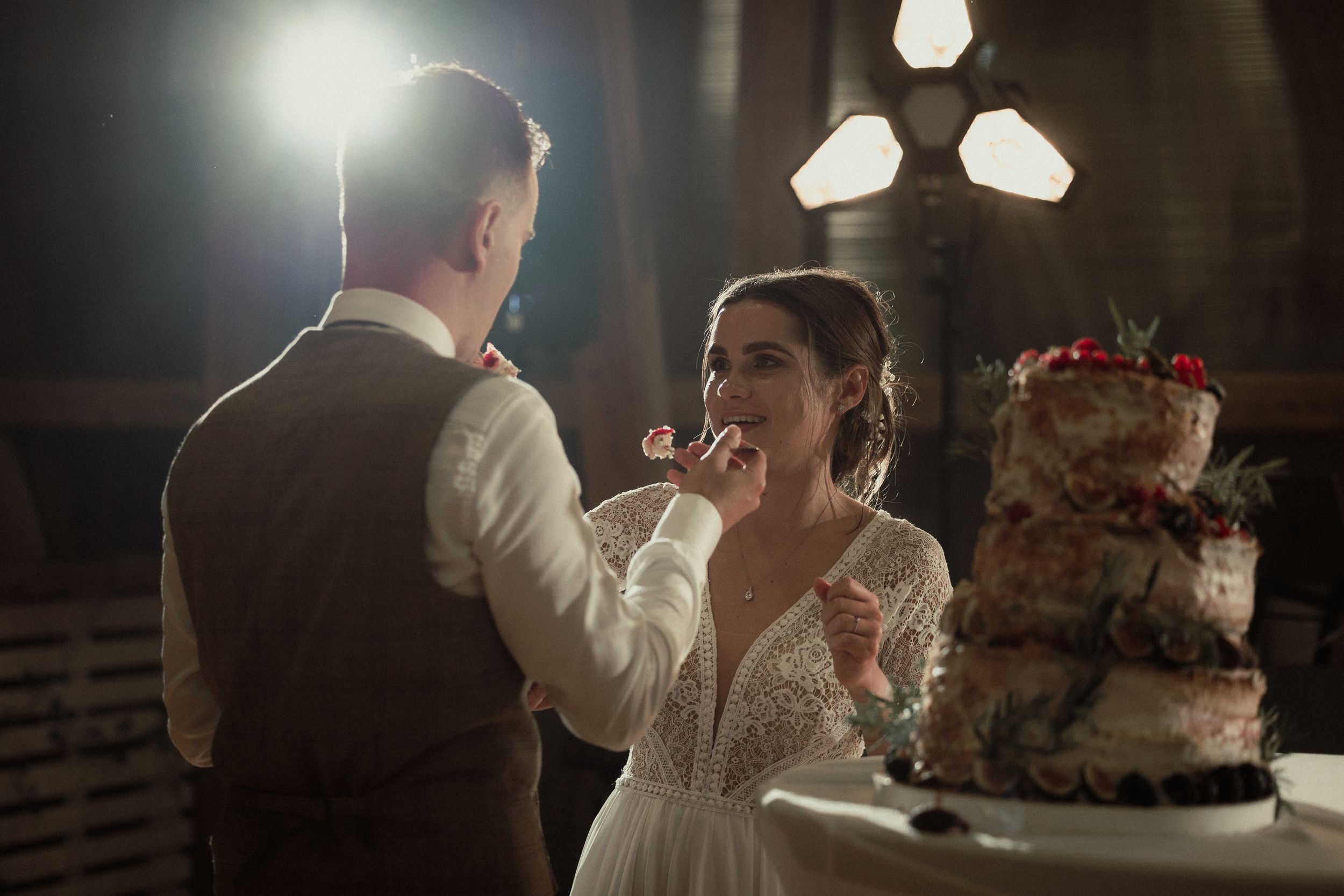 Romantic slow dance at a dimly lit wedding reception with string lights and floral decor in the background.