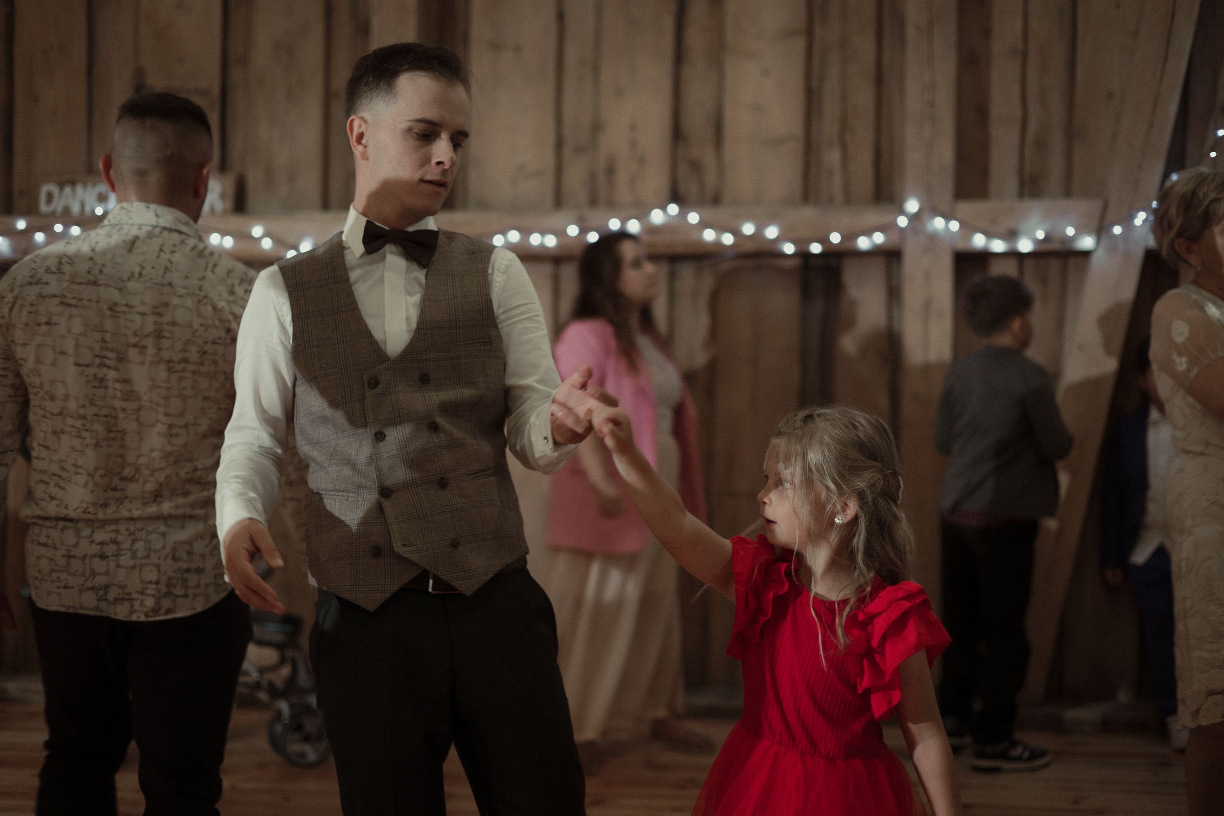 Dancing couples enjoy a romantic evening at a rustic barn venue decorated with twinkling string lights.