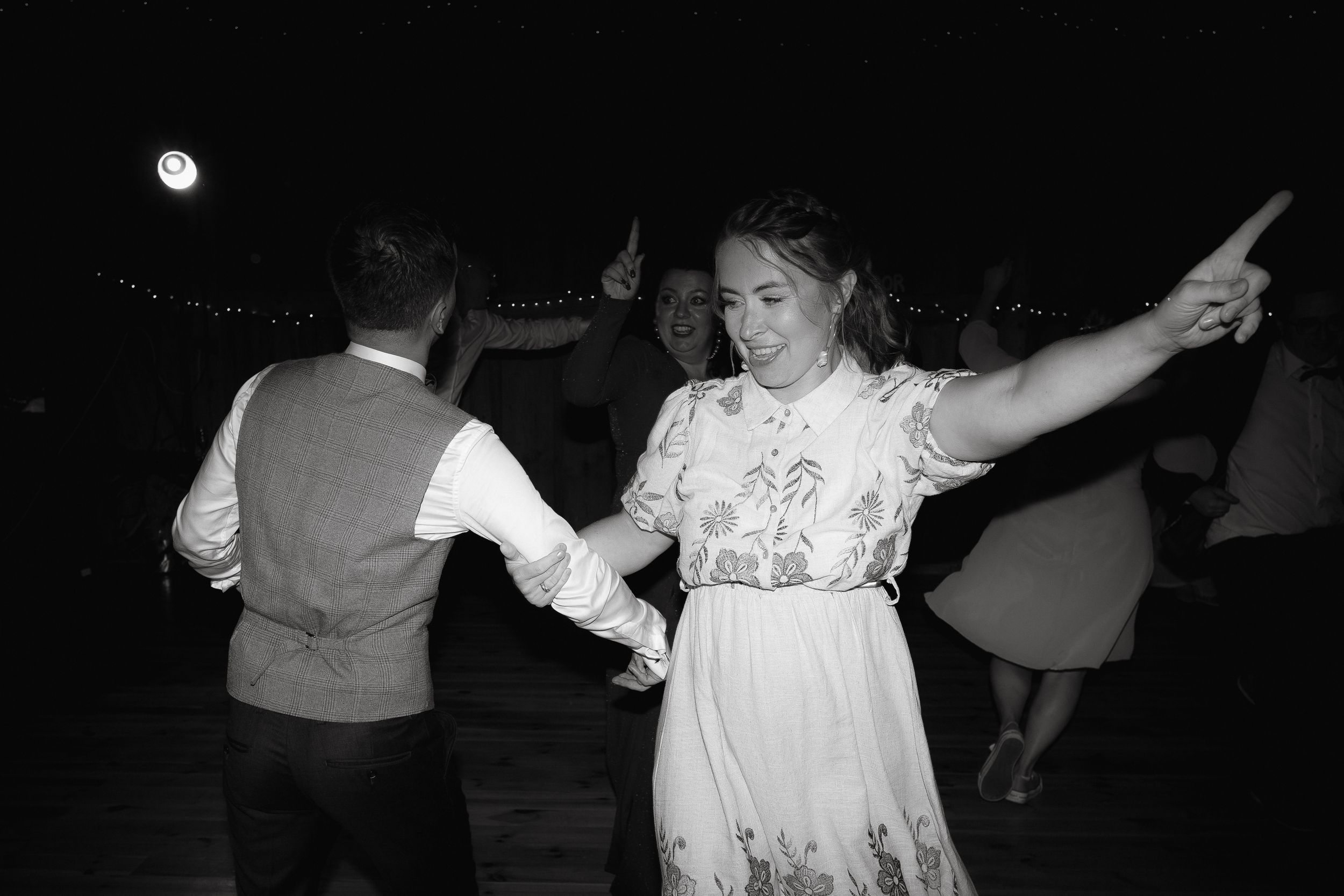 Black and white photo of people dancing joyfully together in vintage clothing with a flash at night.