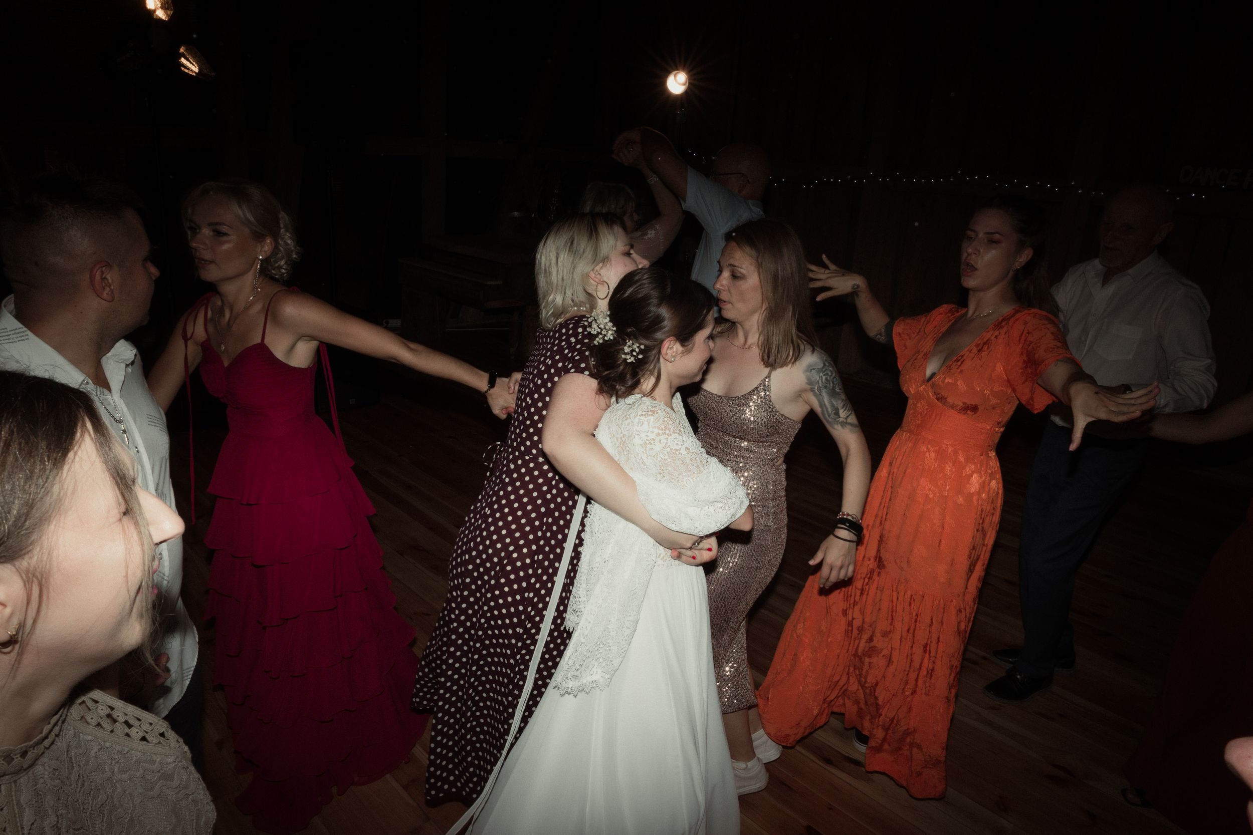 People dancing together in a dark reception hall with various outfits and dresses visible.