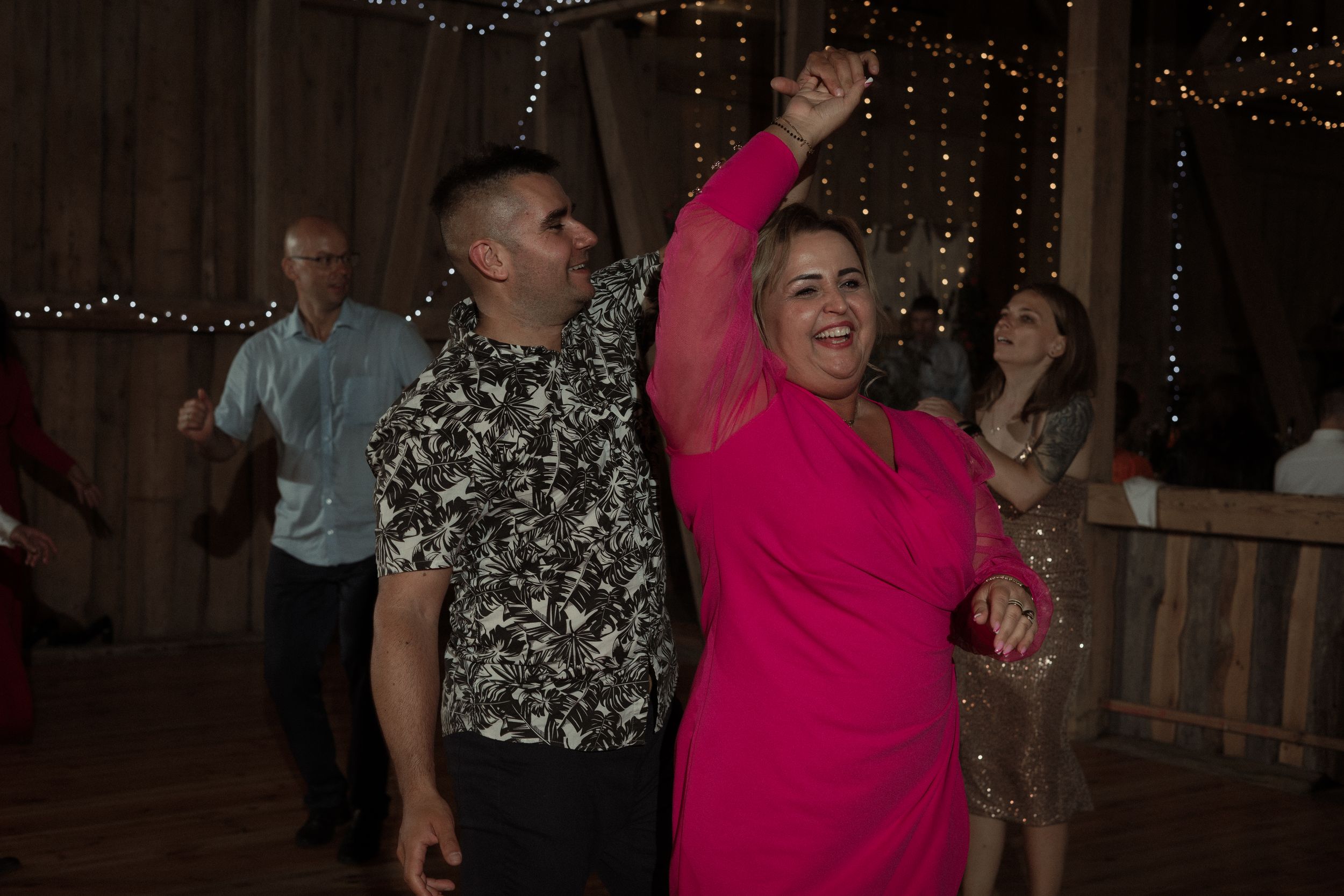 Guests dance and celebrate at a festive party with hanging string lights decorating the dark venue.