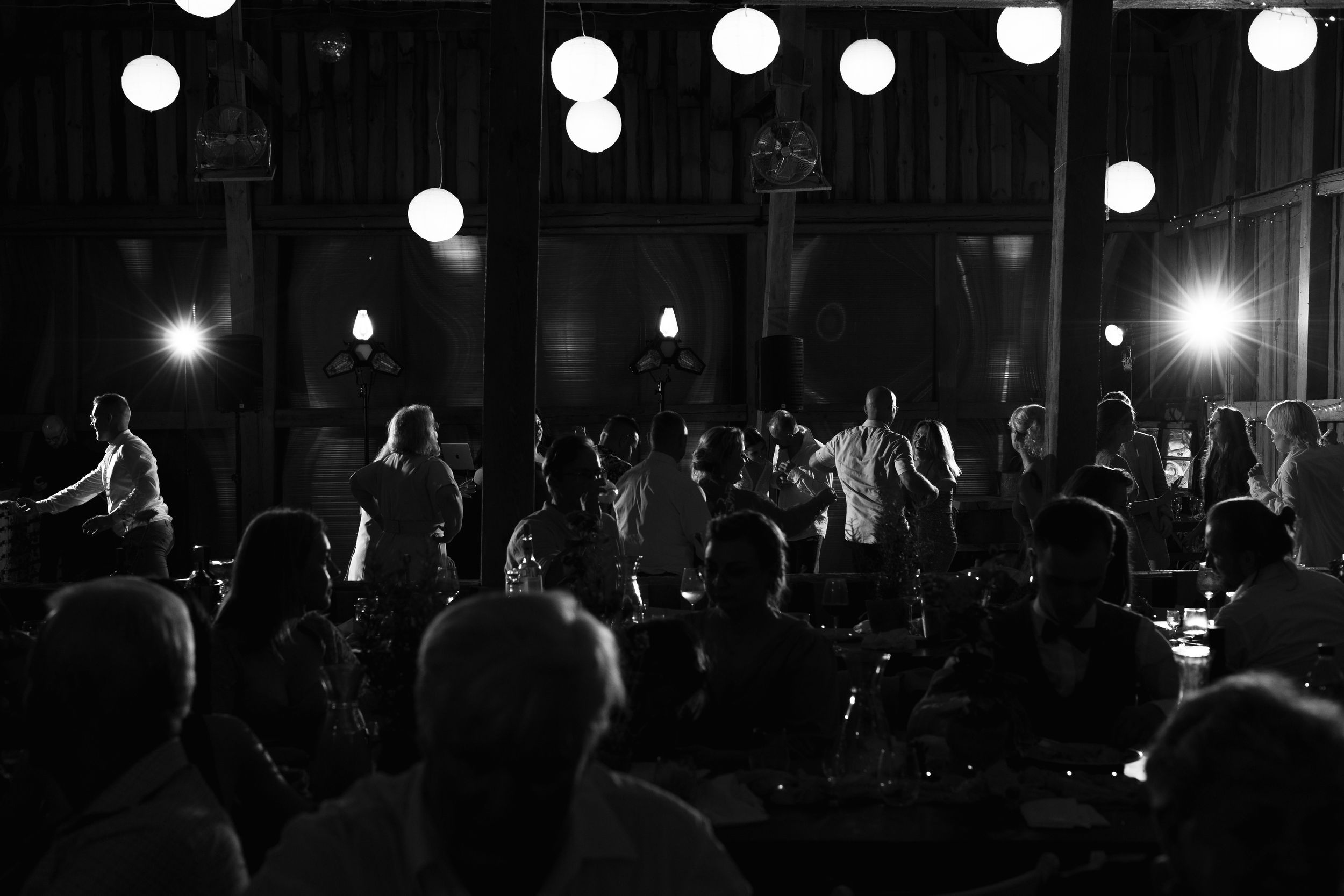 A group of silhouetted people stand in darkness with illuminated glowing lights hanging overhead.