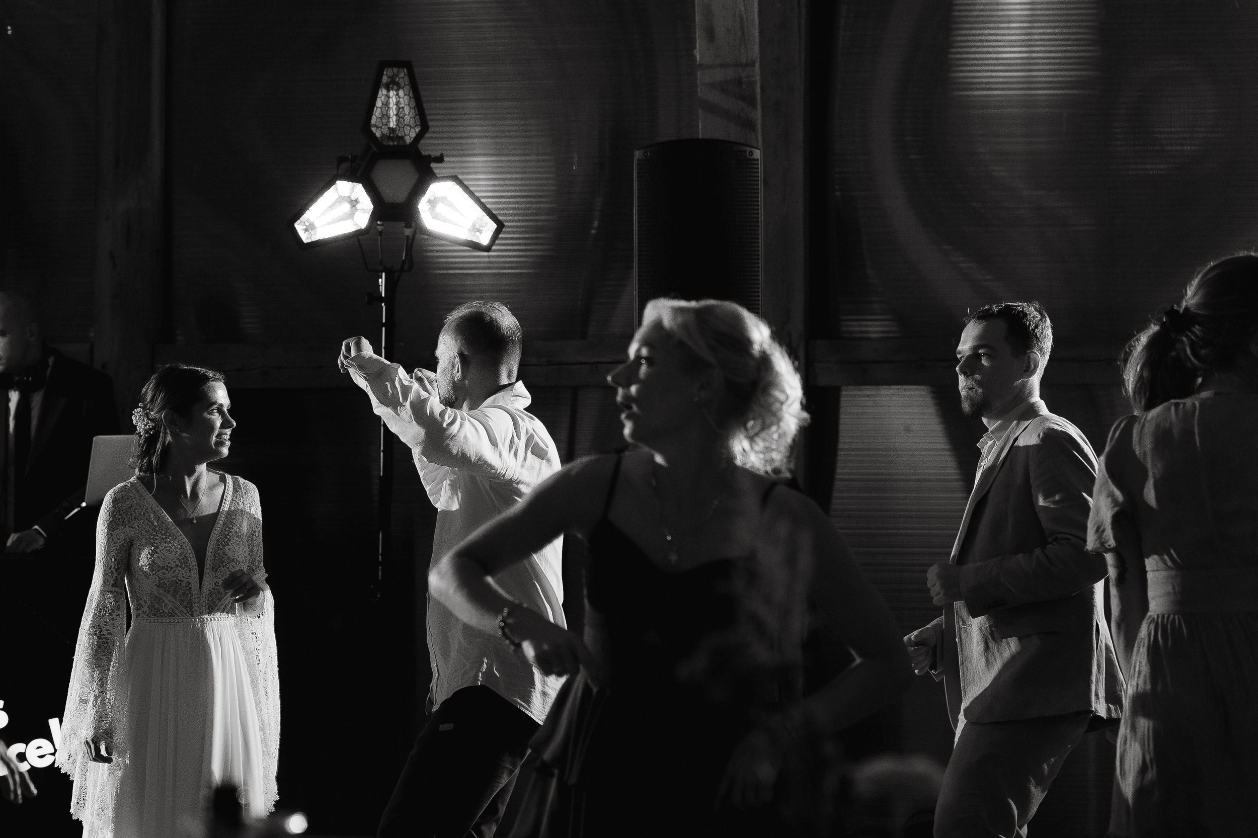 Dance floor crowd celebrating at a dark reception venue with uplighting and dancing silhouettes in the background.