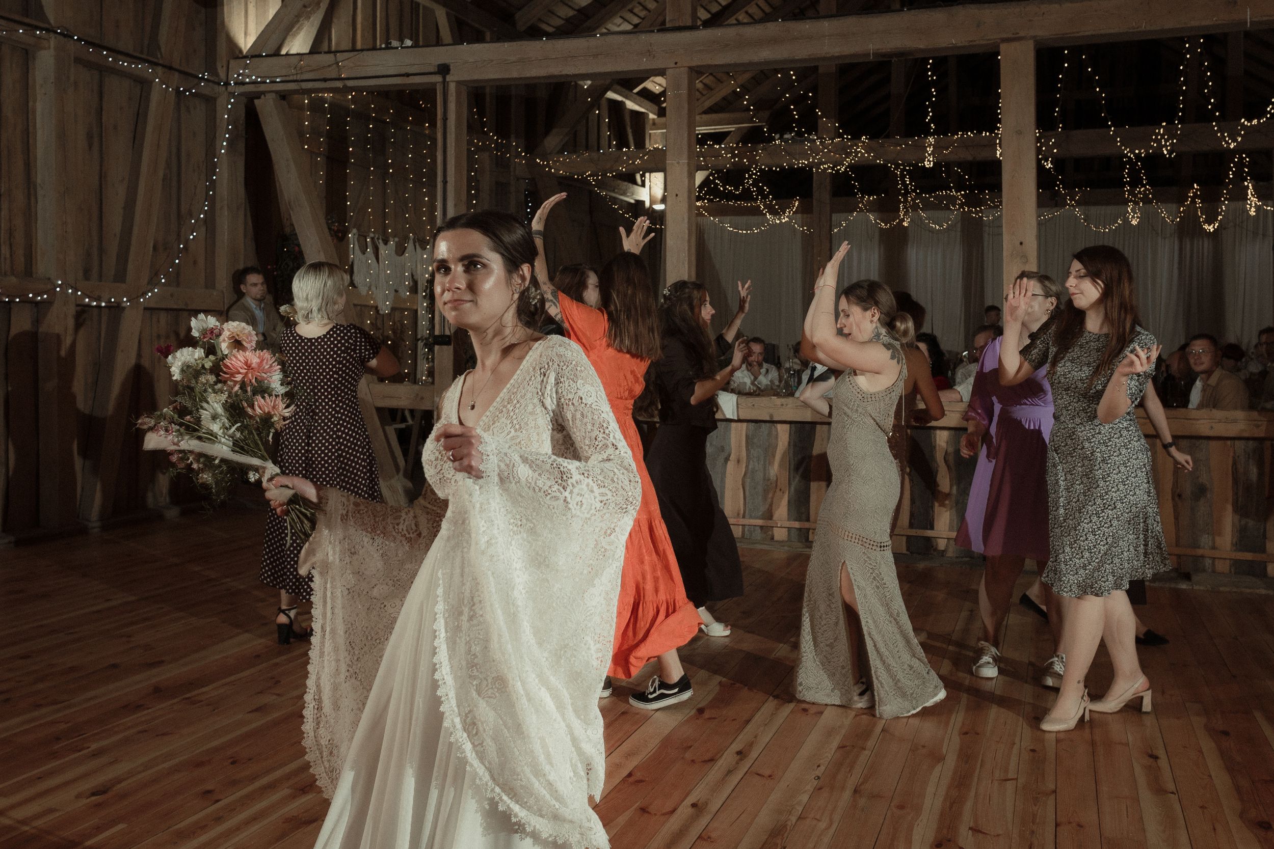 Wedding reception guests dancing and celebrating on a rustic wooden dance floor in a barn venue.