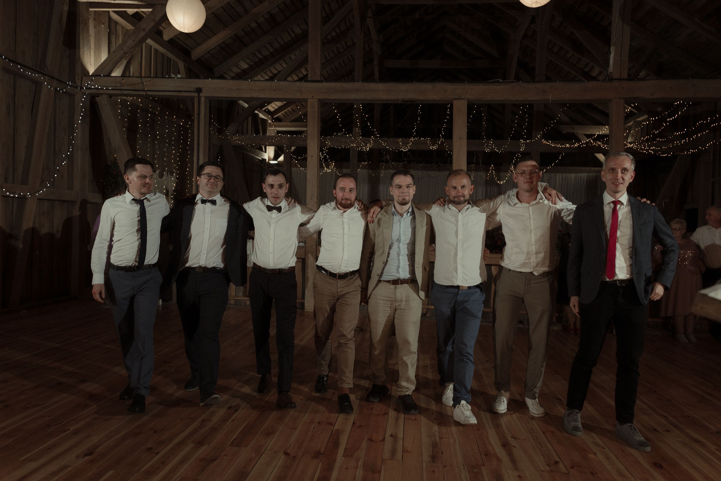 Wedding guests dance at a barn wedding reception under rustic lighting fixtures.